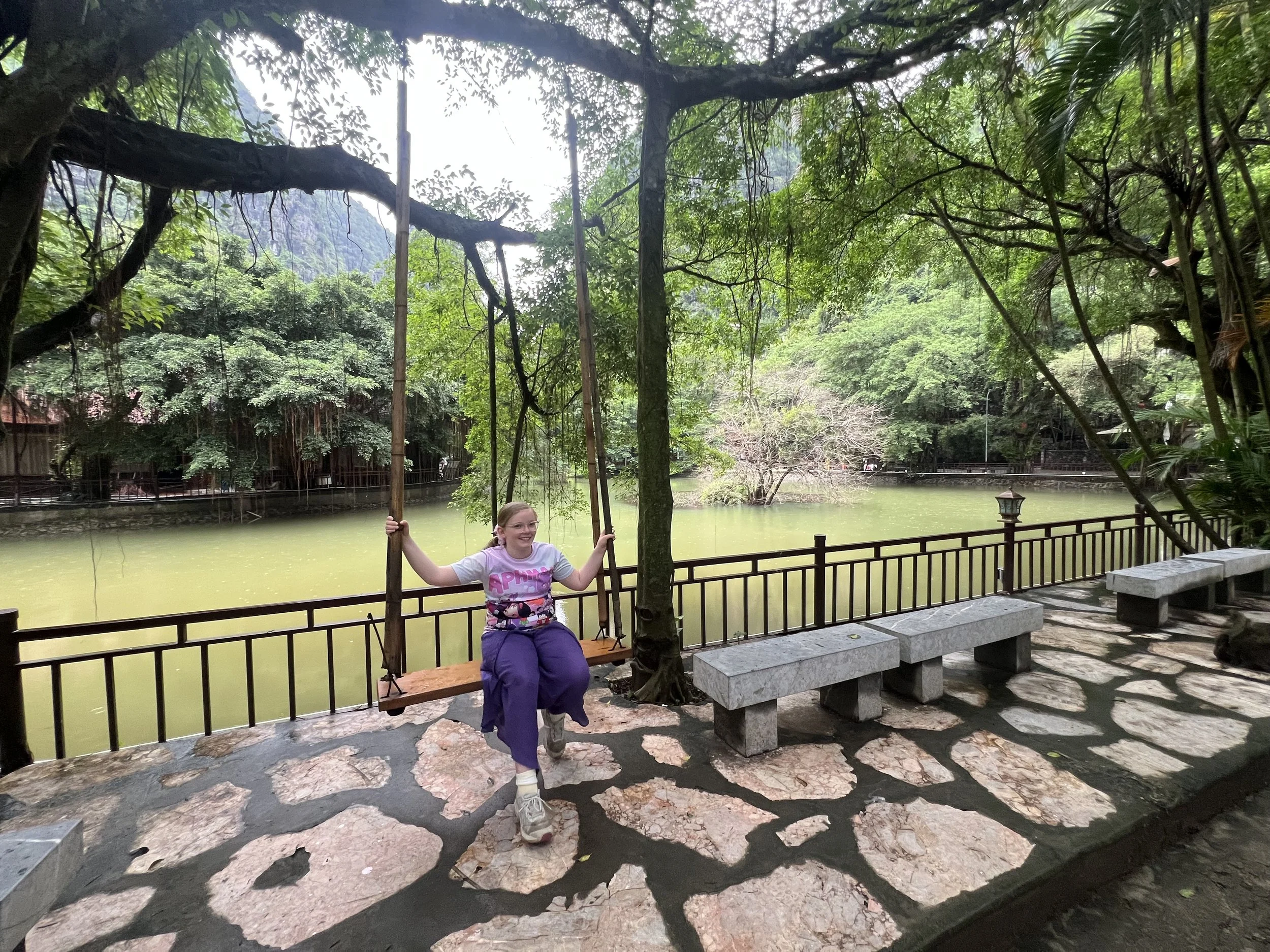 Girl on a wooden swing beside a lake surrounded by limestone hills in Ninh Binh