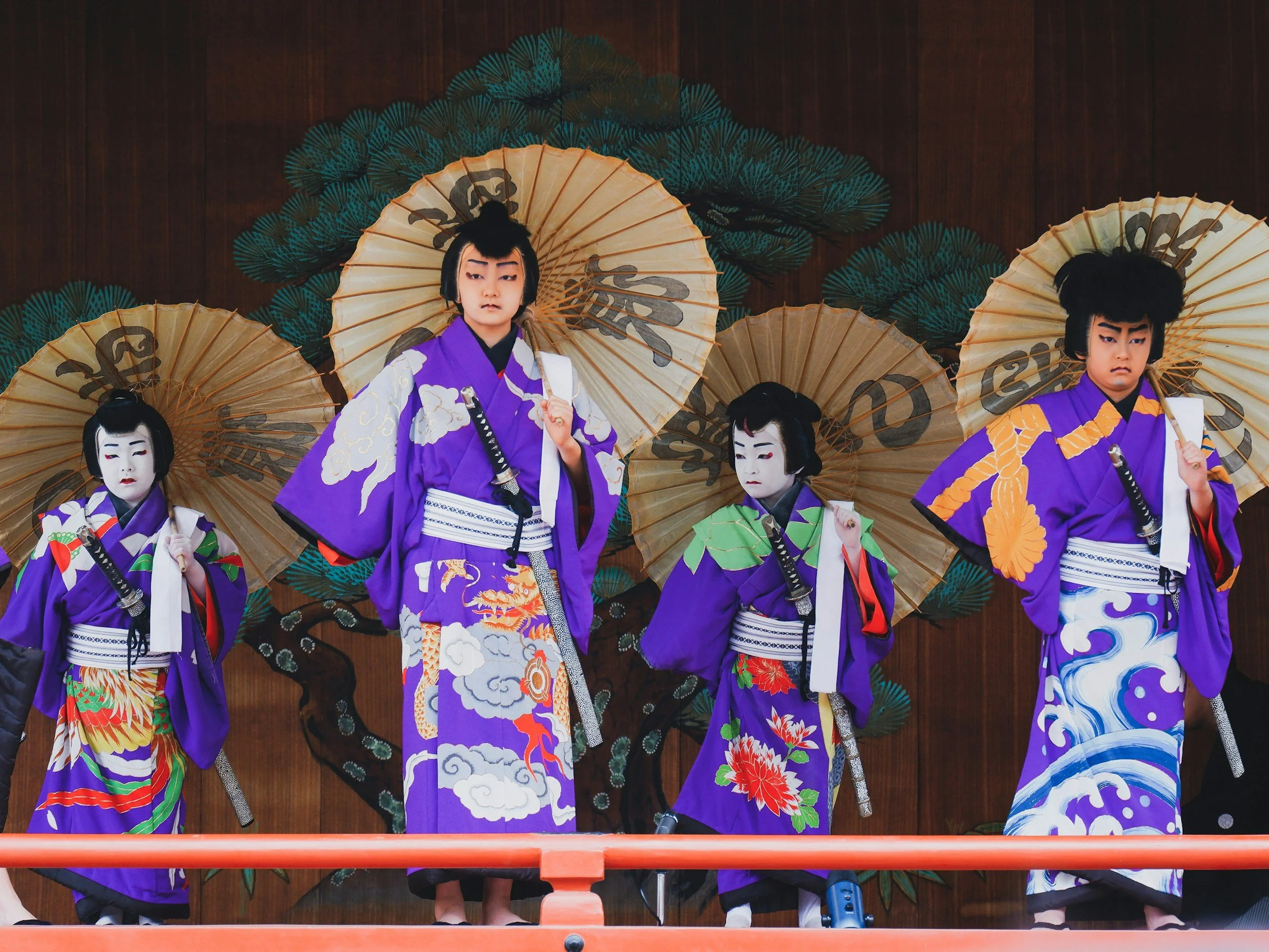 Young performers in purple kimono with paper parasols at a traditional Japanese stage performance