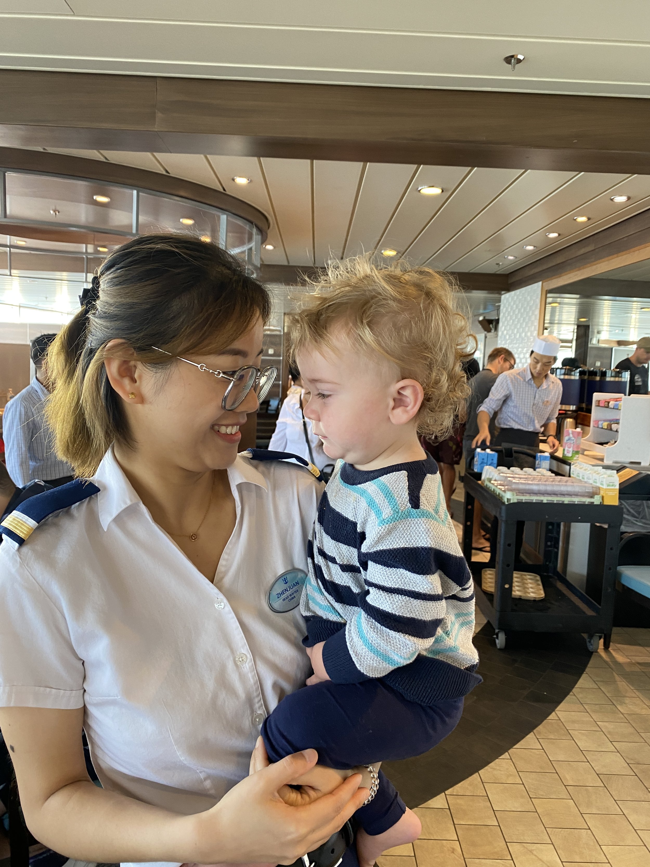 Royal Caribbean crew member holding a smiling toddler in the dining room on a family cruise