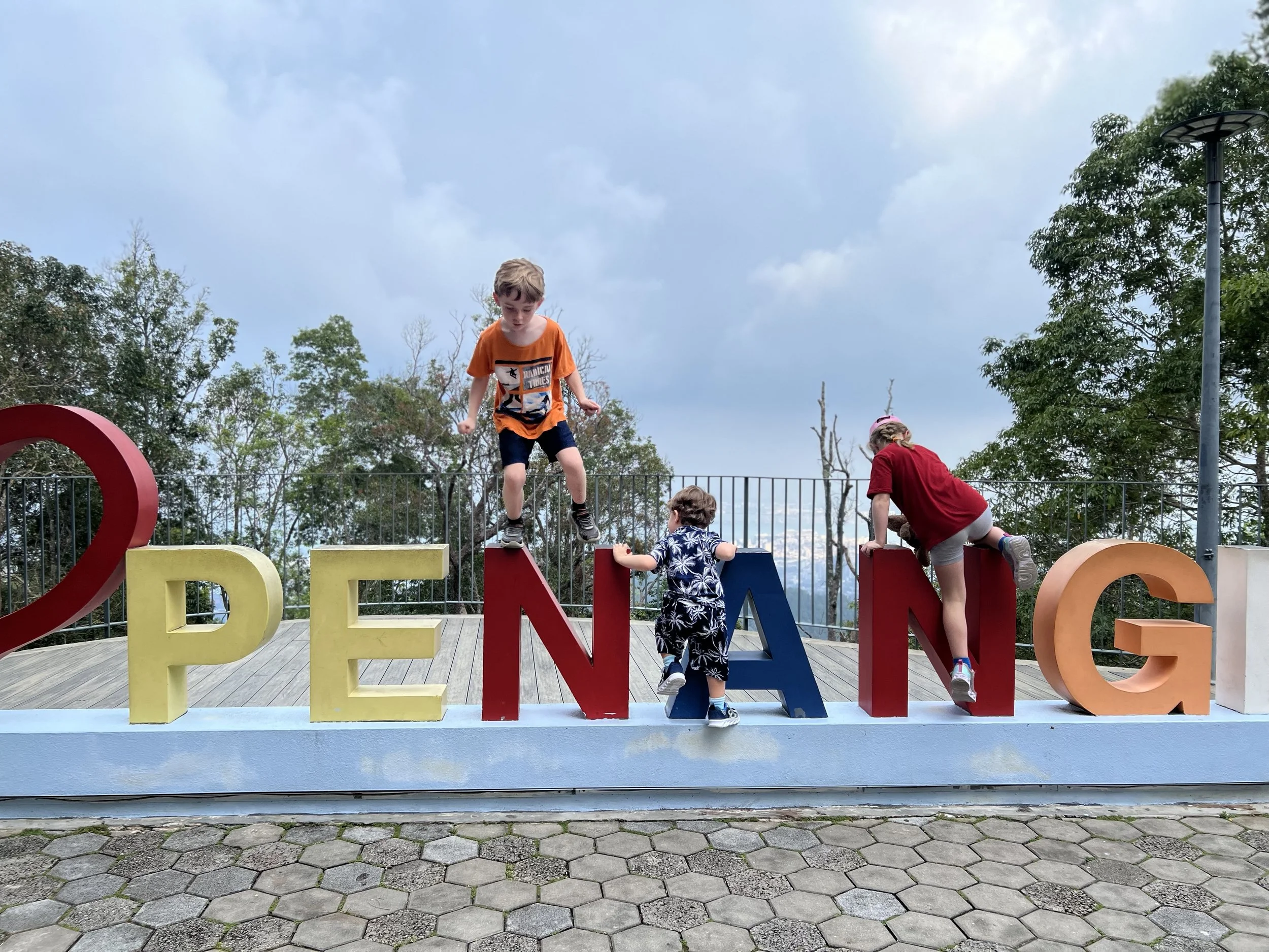 Three worldschooling kids climbing the giant Penang letters sign in Malaysia