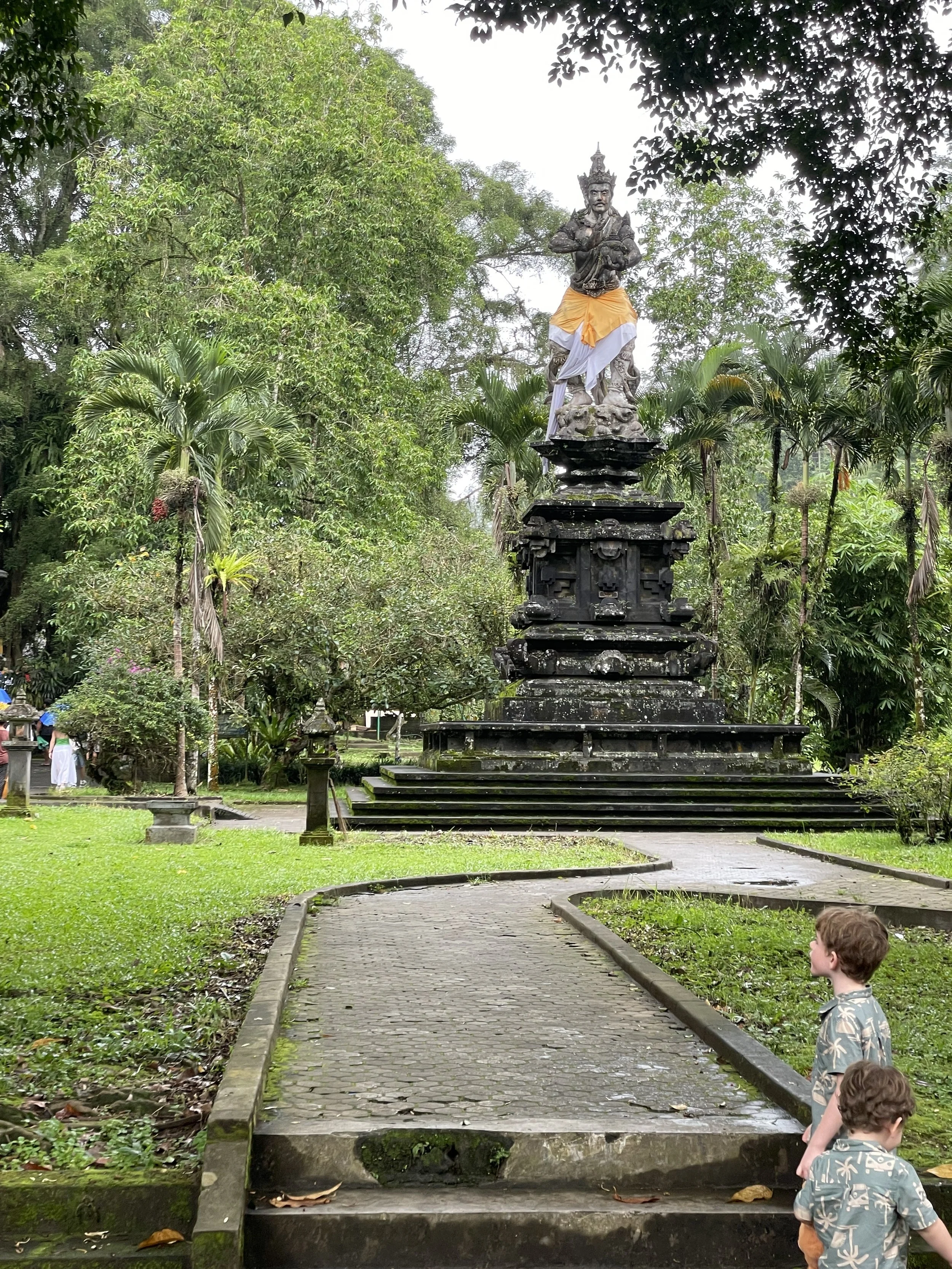 Two boys looking up at a stone Balinese temple shrine in a garden in Bali