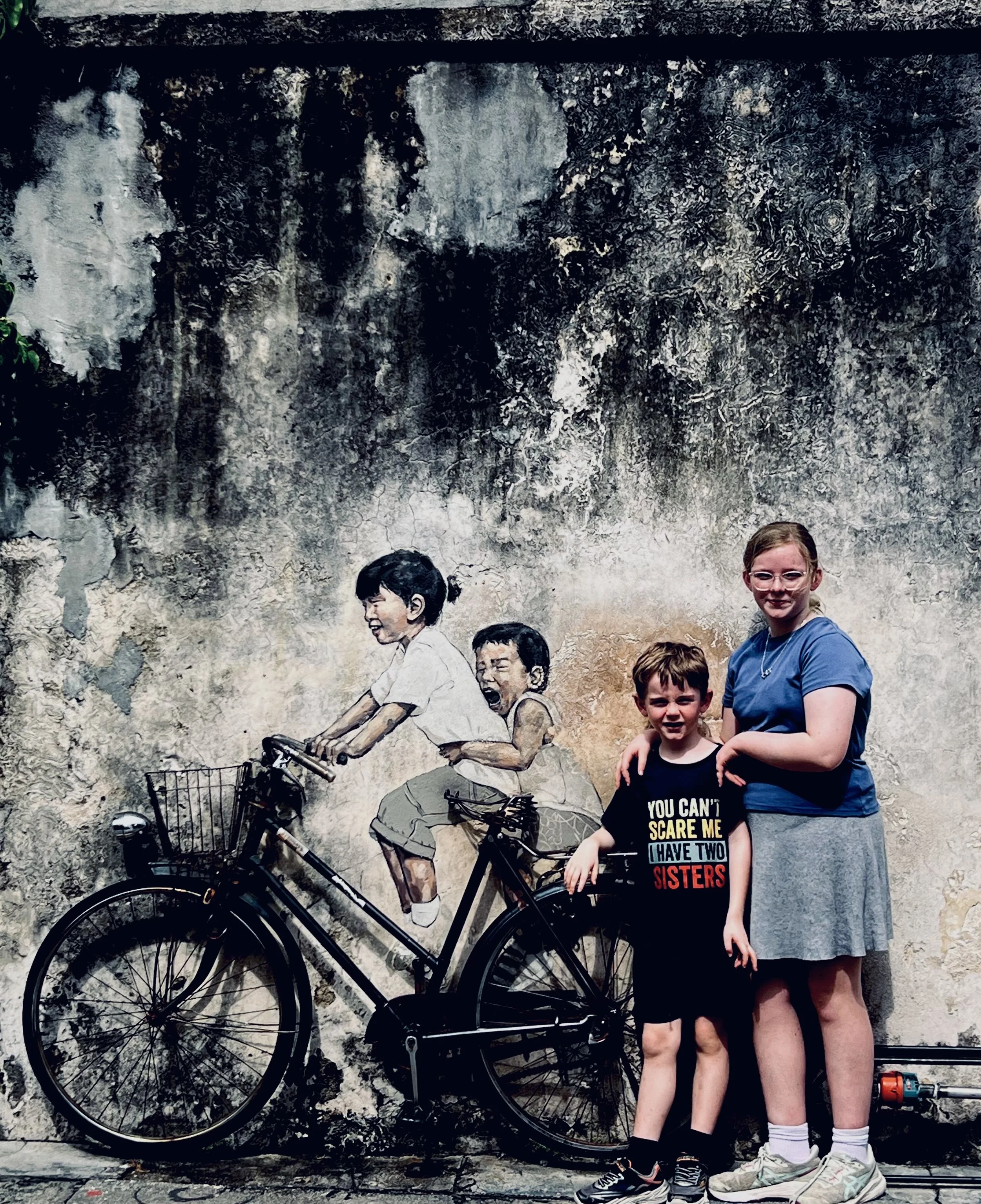 Kids posing with the famous Children on a Bicycle street art mural in George Town, Penang