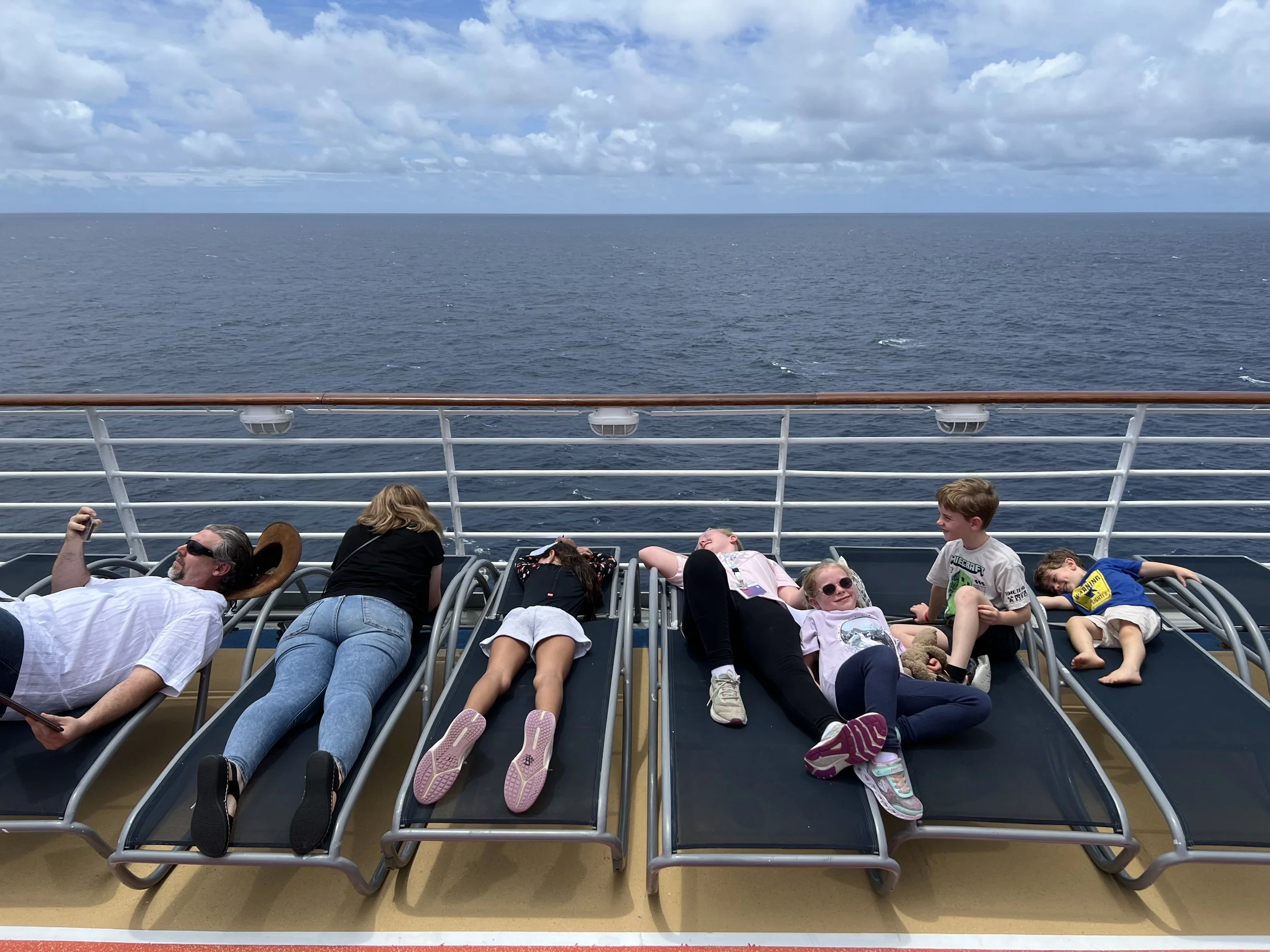 Families lying on sun loungers on the cruise ship deck looking out to the ocean on a sea day