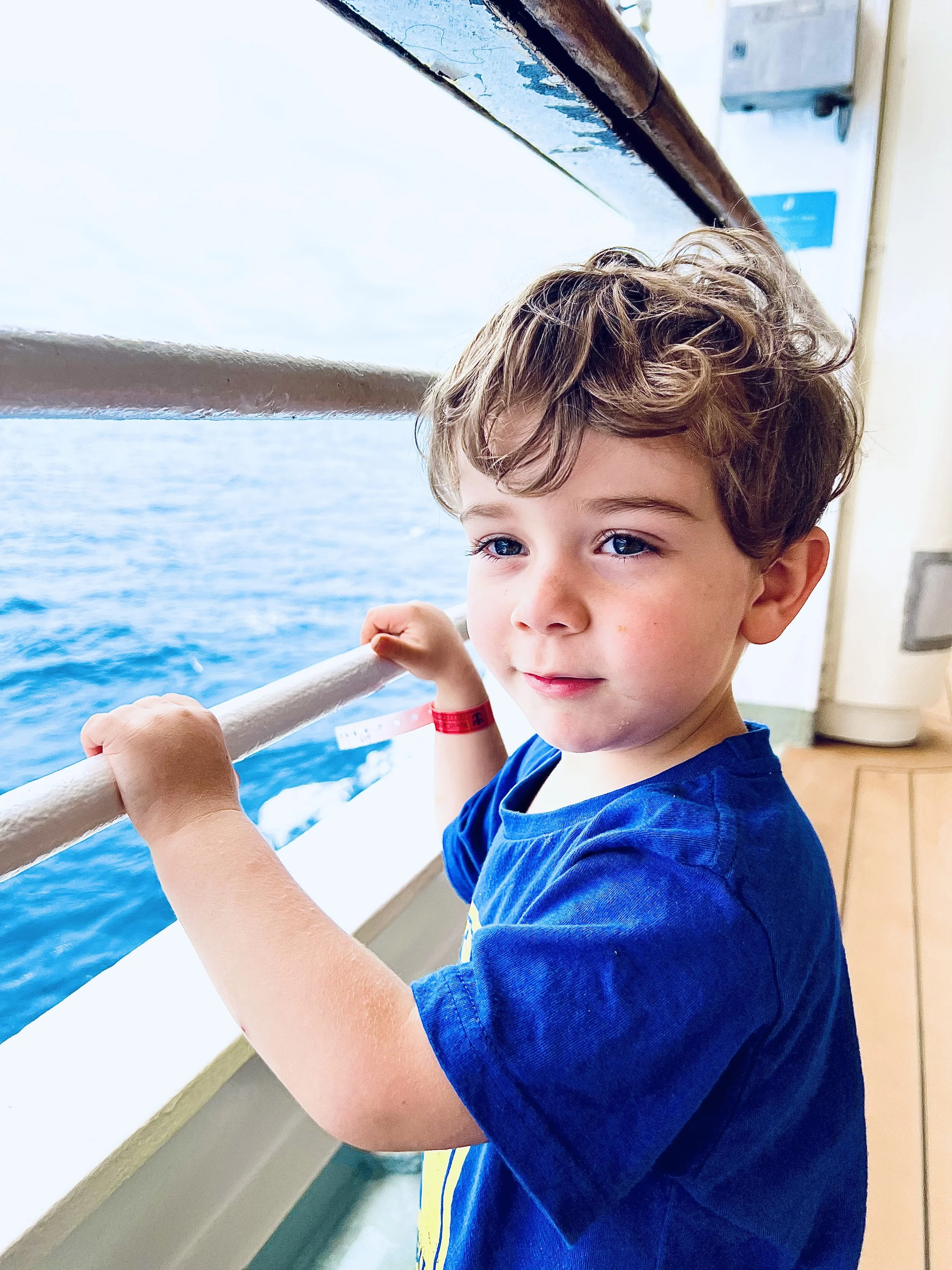 Young boy with curly hair gazing out to sea from the ship's rail on a family cruise