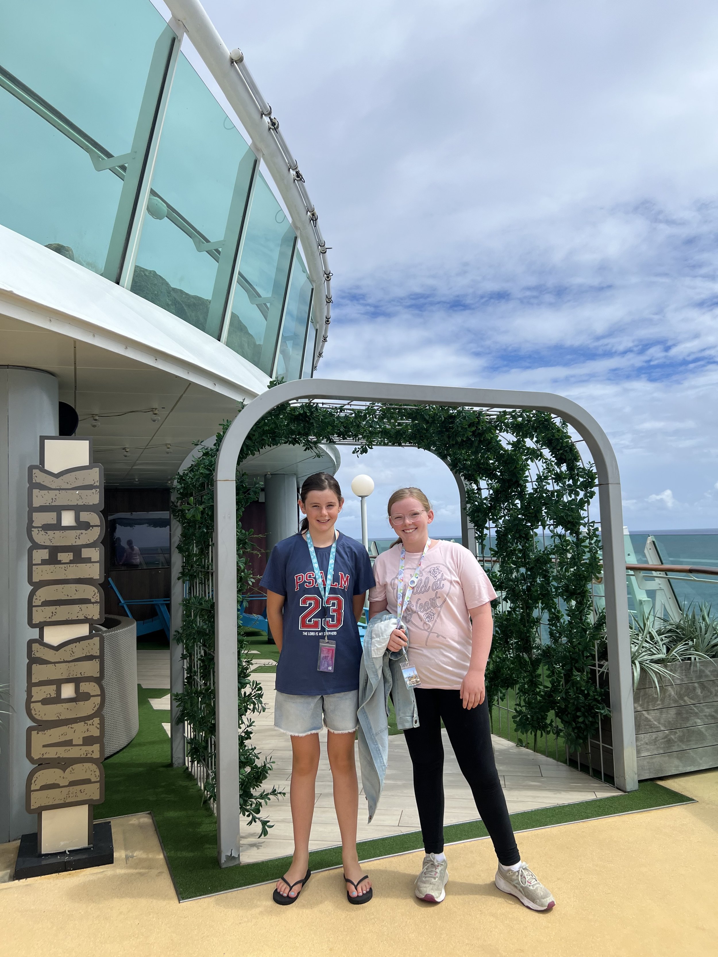 Two worldschooling girls standing under a green garden arch on the cruise ship deck