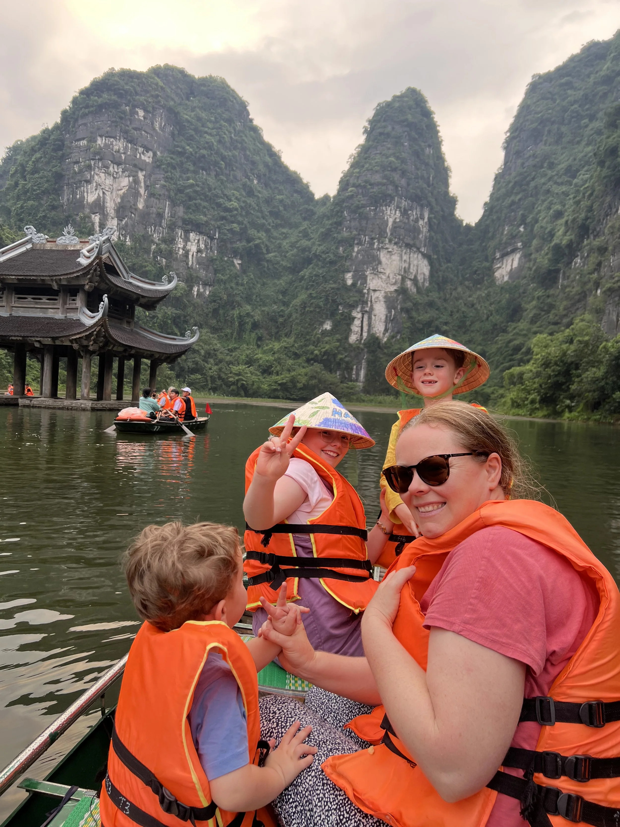 Girl in a conical hat in front of a pagoda and limestone karsts at Trang An, Ninh Binh