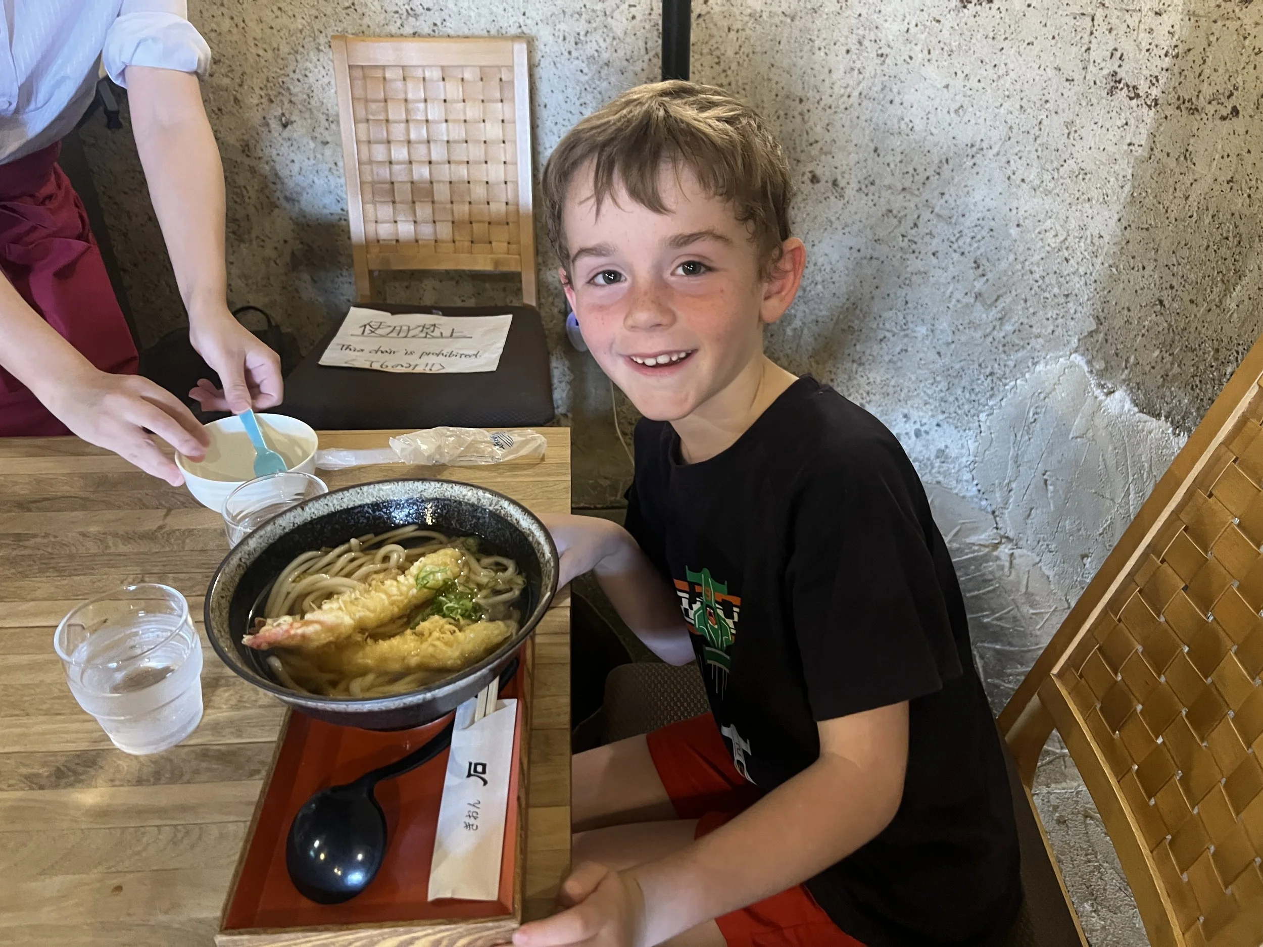 Smiling boy with a bowl of tempura udon noodles at a restaurant in Japan