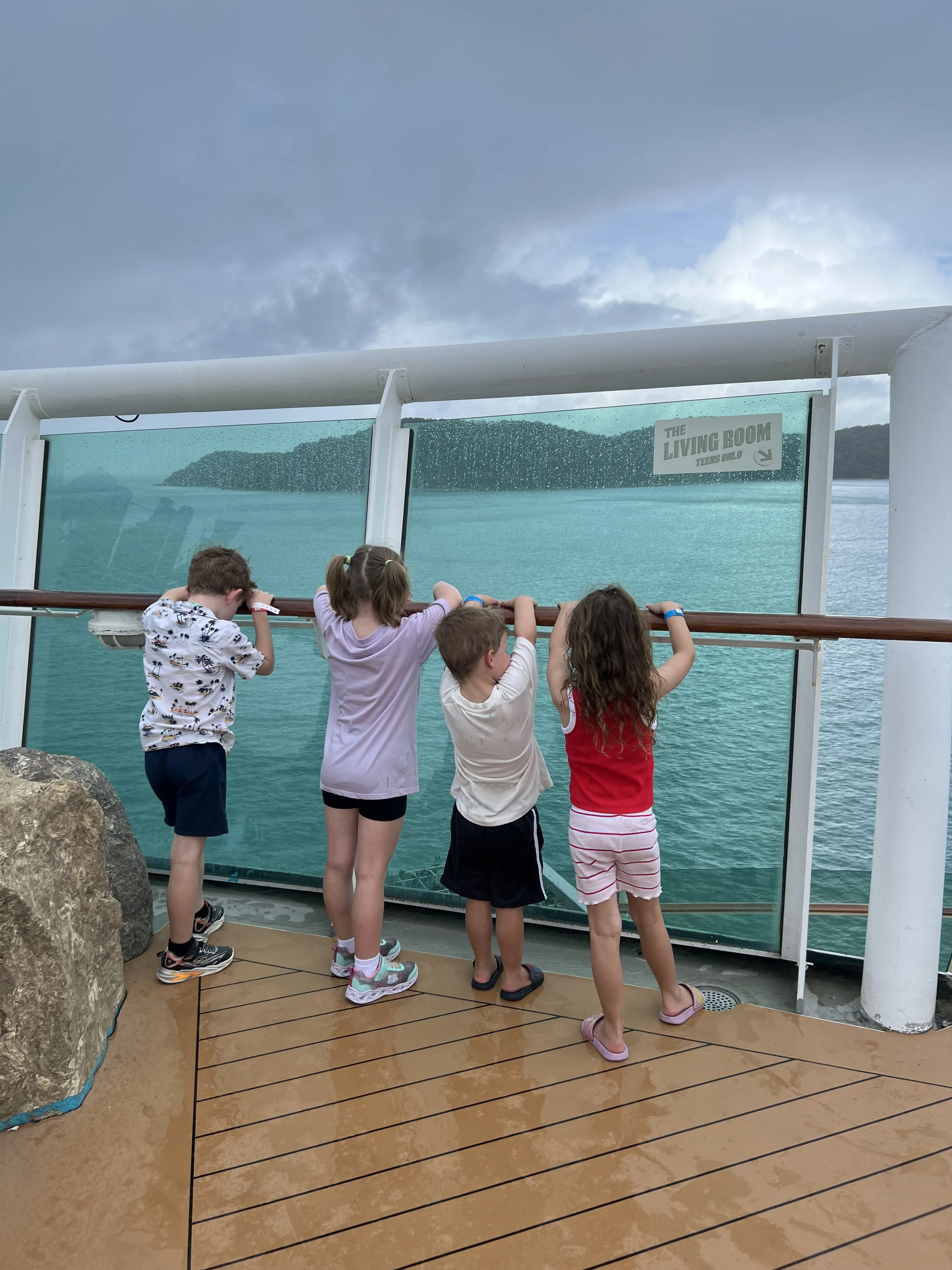 Four kids looking out over the sea from the ship's deck railing as the cruise sails through Asia