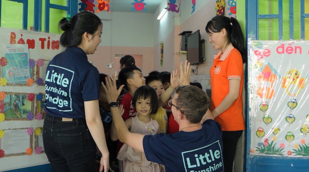 Little Sunshine Pledge volunteers high-fiving with children at a Vietnamese orphanage