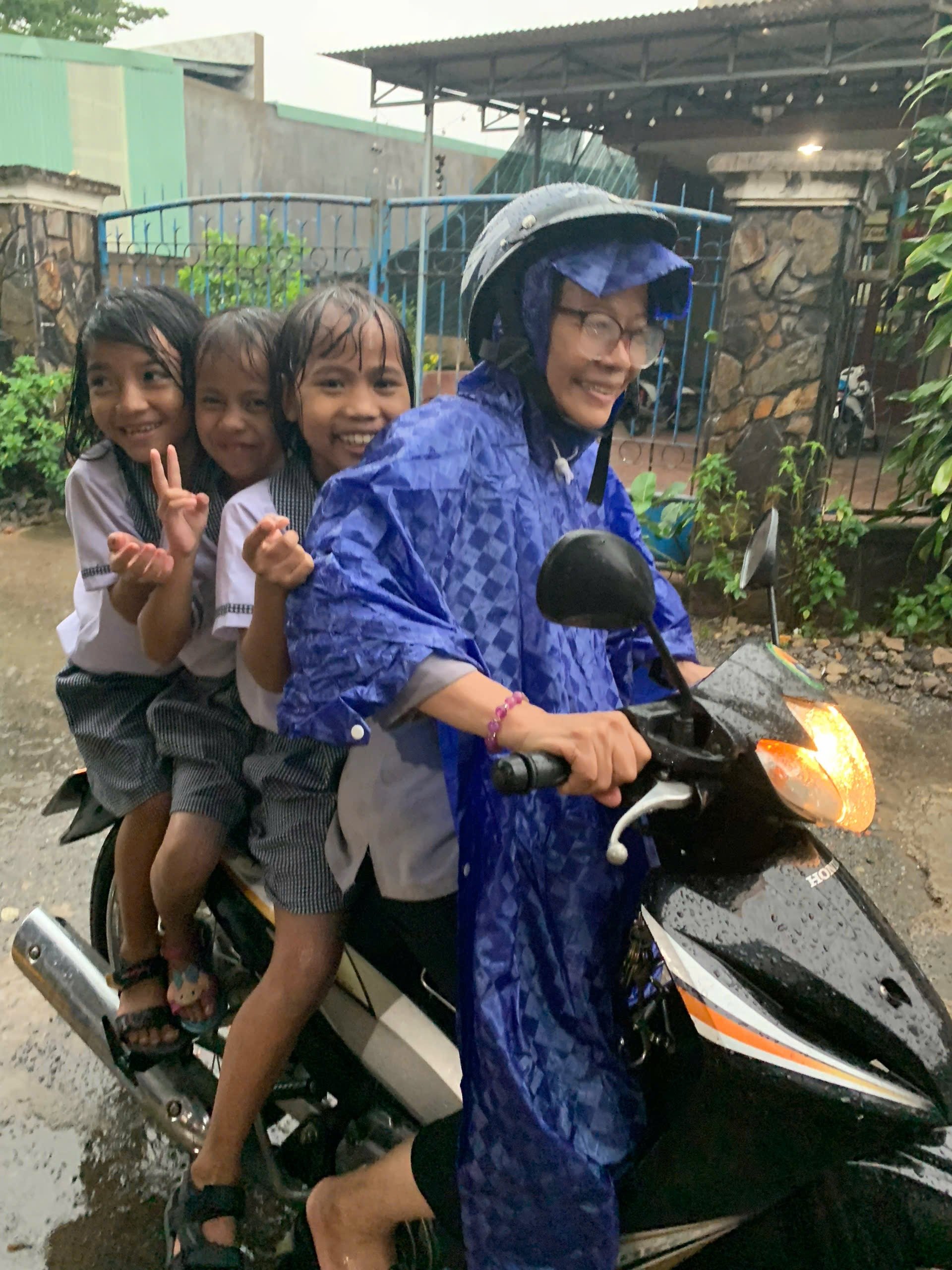 Photo shows Ms. My riding her Honda Wave scooter in the rain to drop off 3 kids to school