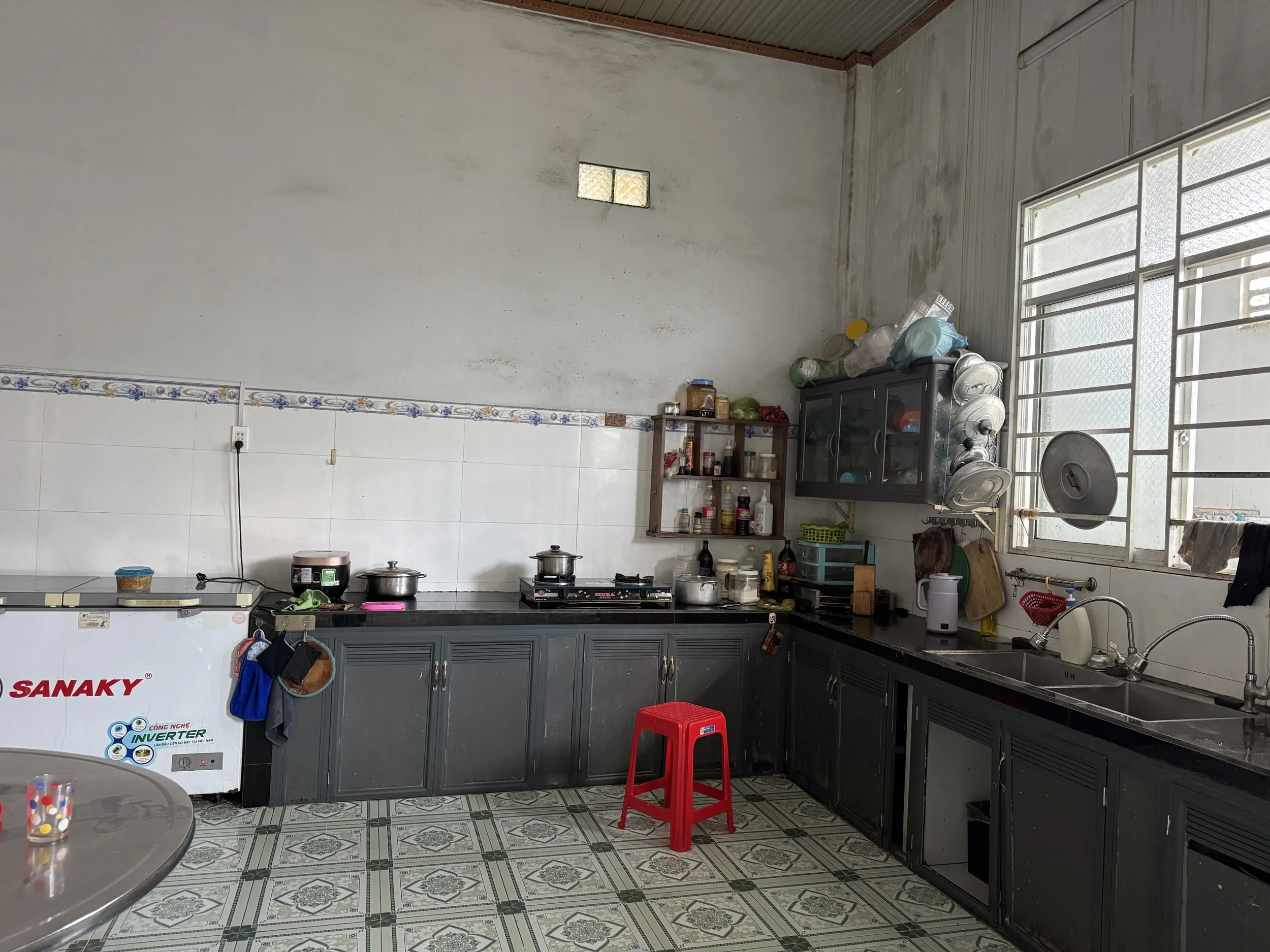 Photo showing the kitchen of the orphanage with benches visible, basic cooking utilities and the red stool