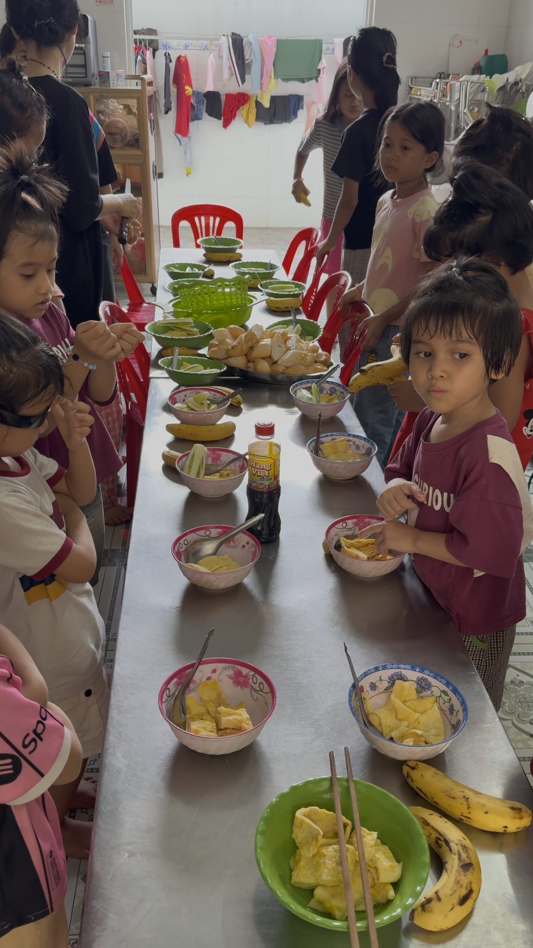 A group of kids with bowls with food laid out in front of them on a long table