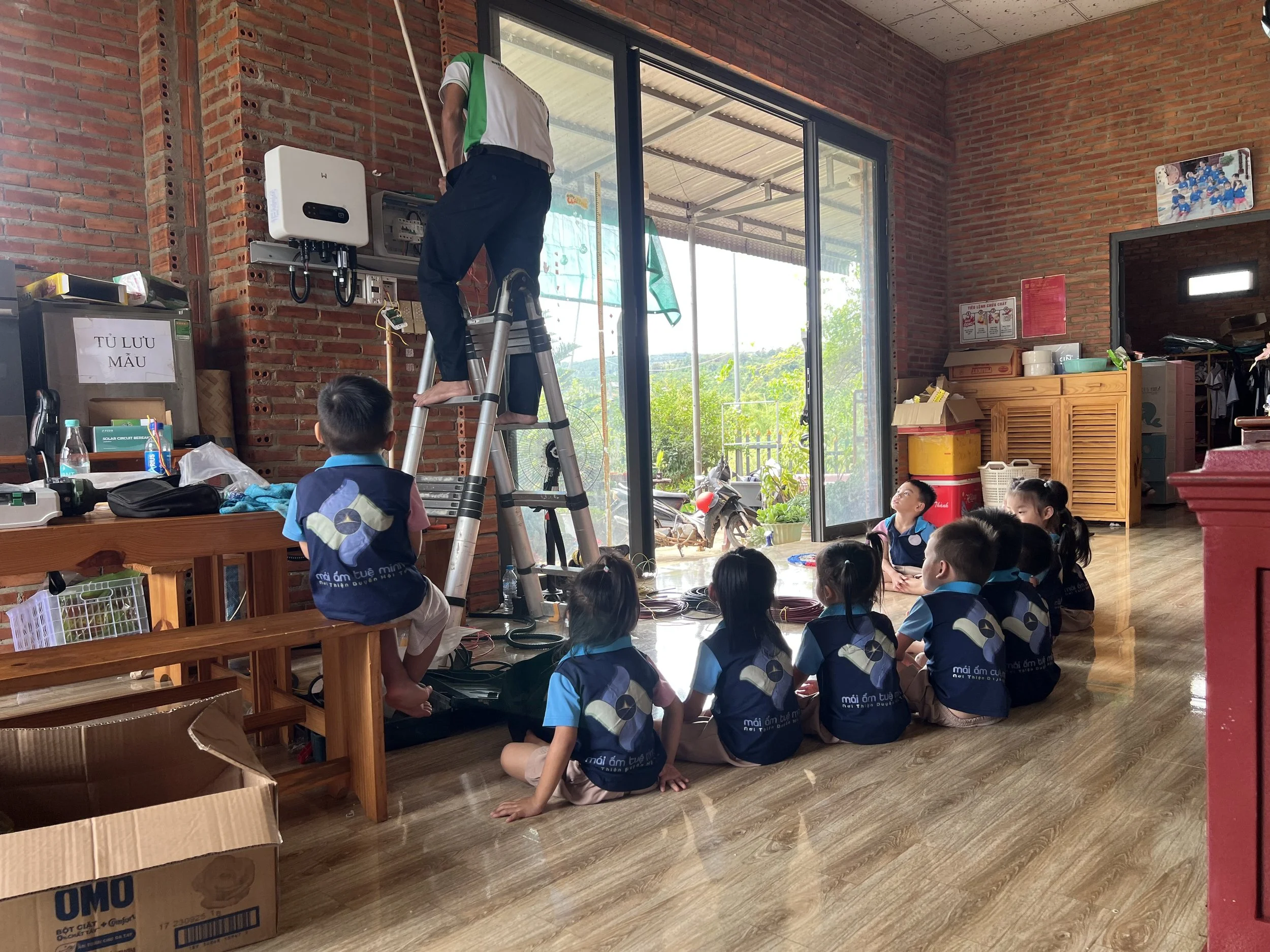 Children at an orphanage watching the Little Sunshine Pledge team install a GoodWe solar inverter on the wall
