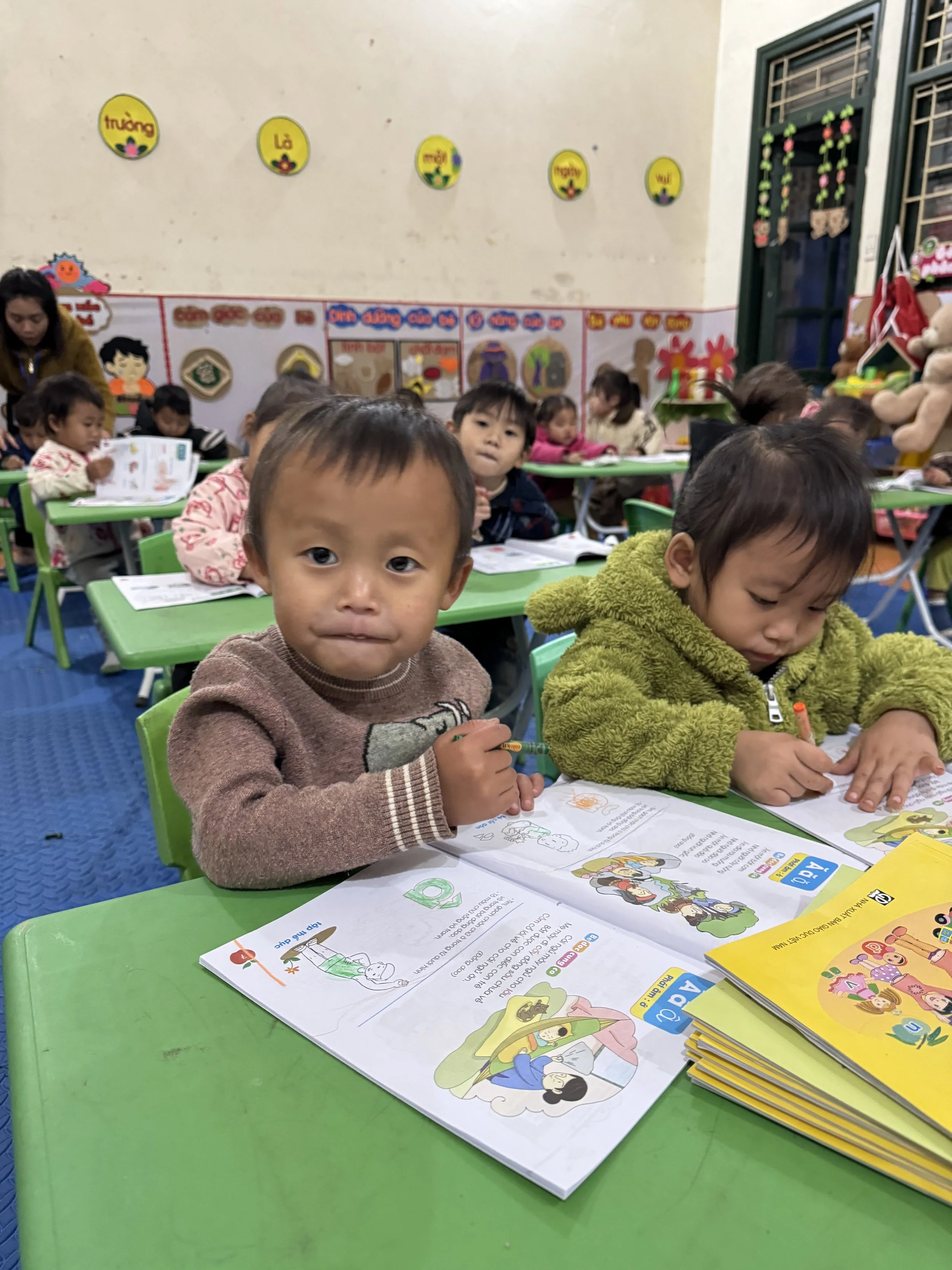 Young children studying and drawing at desks in a brightly lit kindergarten classroom powered by solar energy