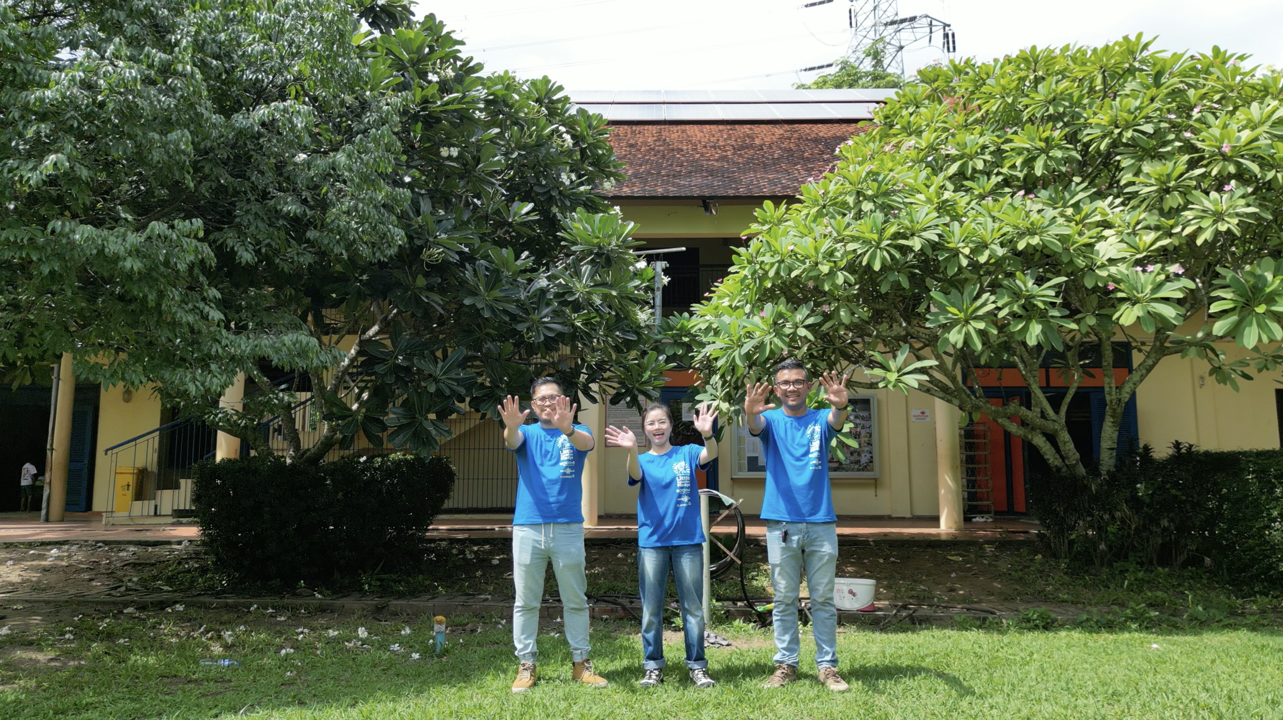 Little Sunshine Pledge team standing in front of a building from Sunrise Cambodia with panels shining on the roof in the background