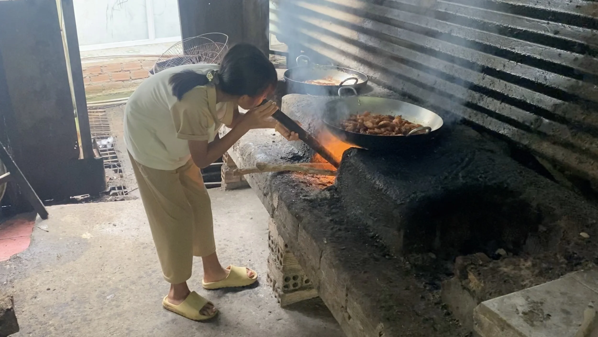 Child cooking over a wood-fired stove in a basic outdoor kitchen at a Vietnamese orphanage before solar installation