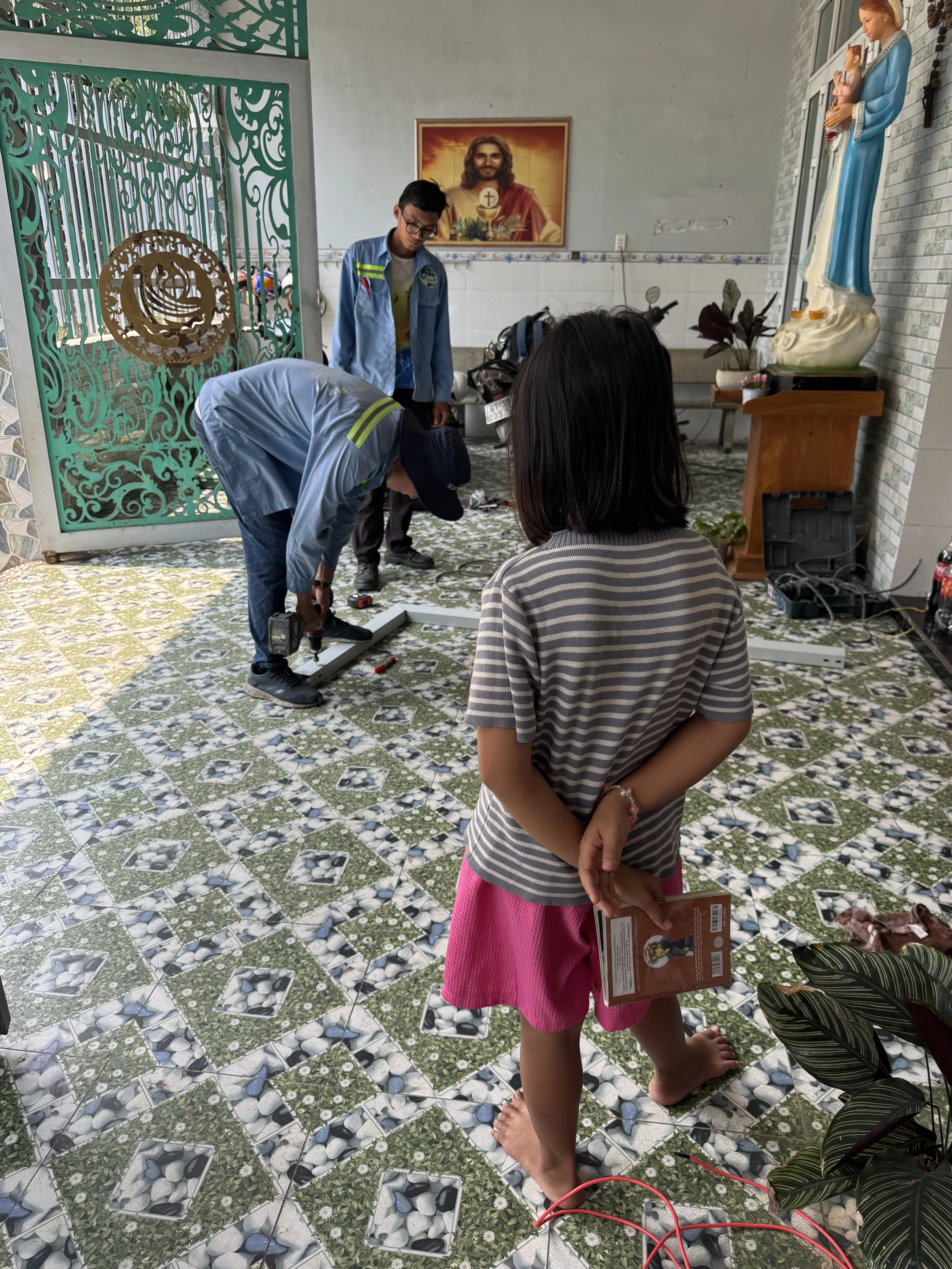 A child with a book in her hand is watching while installers are preparing the channel for the electrical cabling to go on the wall
