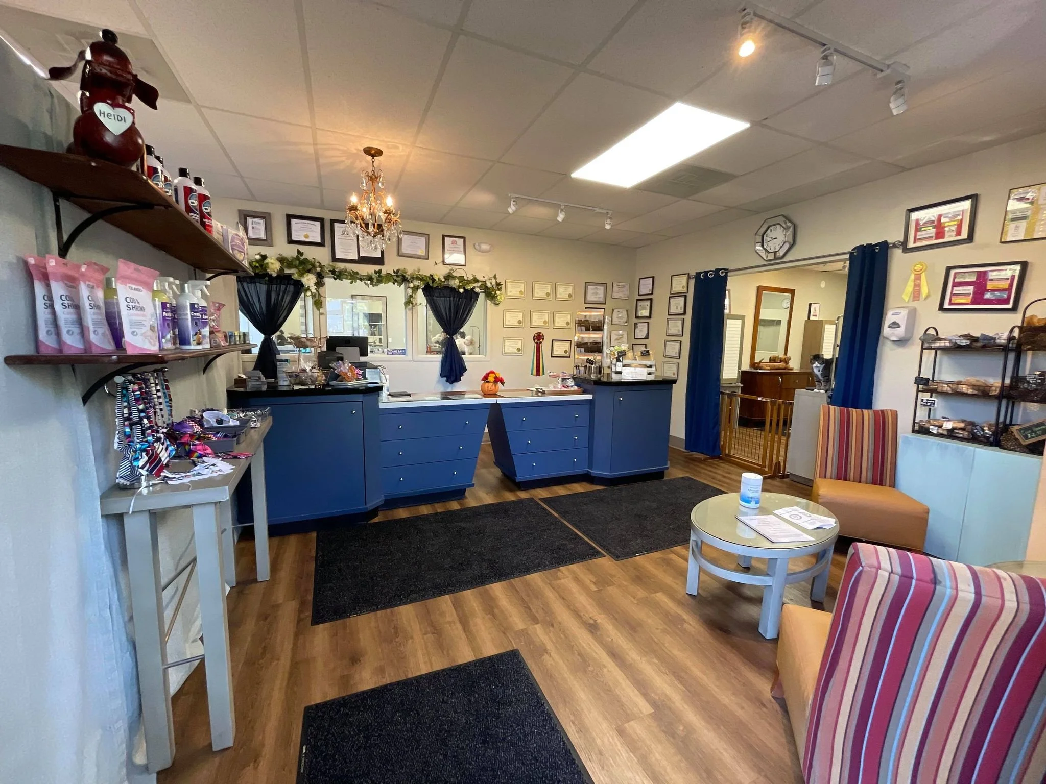 Interior of a reception area with blue counter, framed certificates on walls, striped armchairs, a small round table, and shelves with various products.