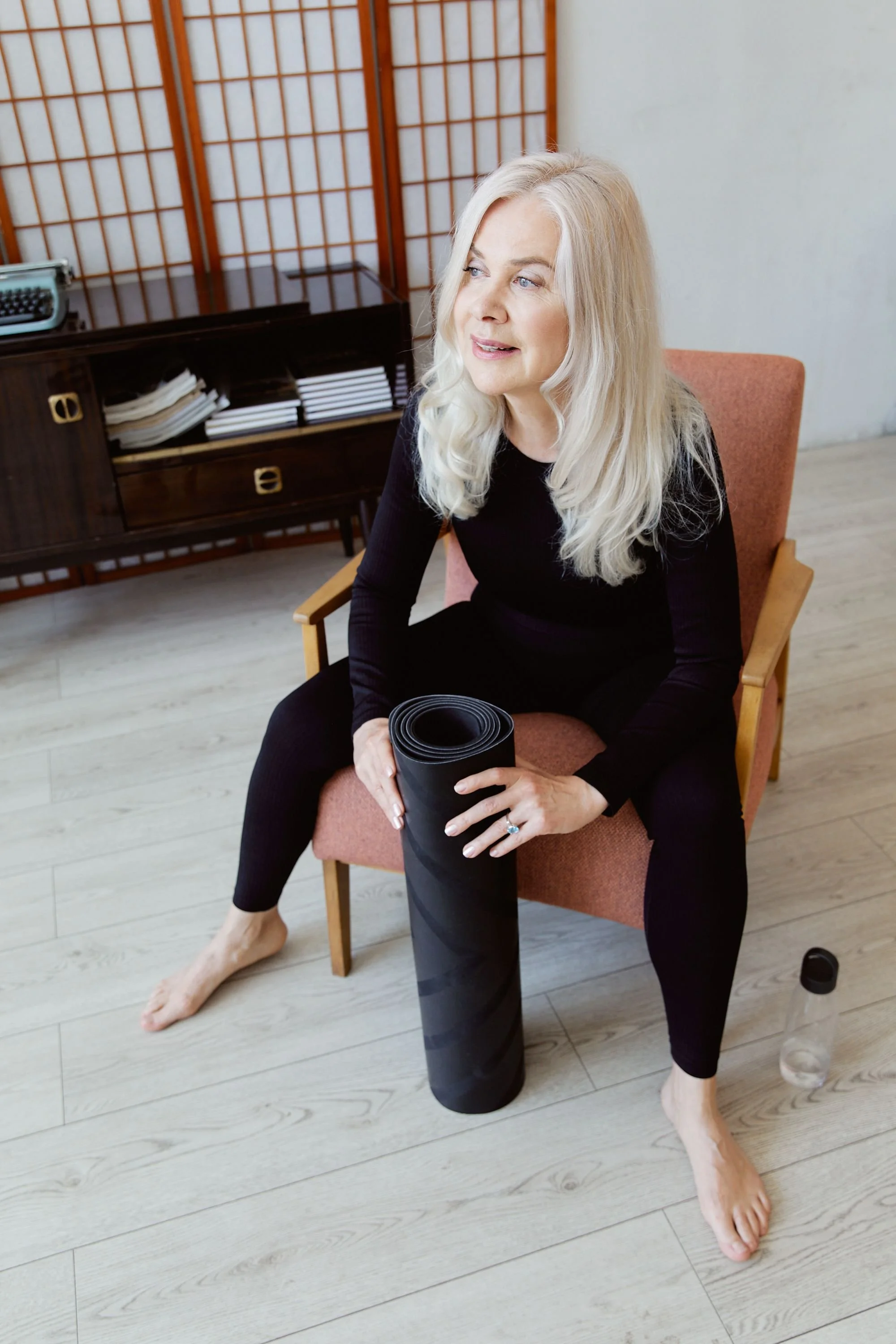 "Woman in her 50s relaxing with a yoga mat, calm morning routine"