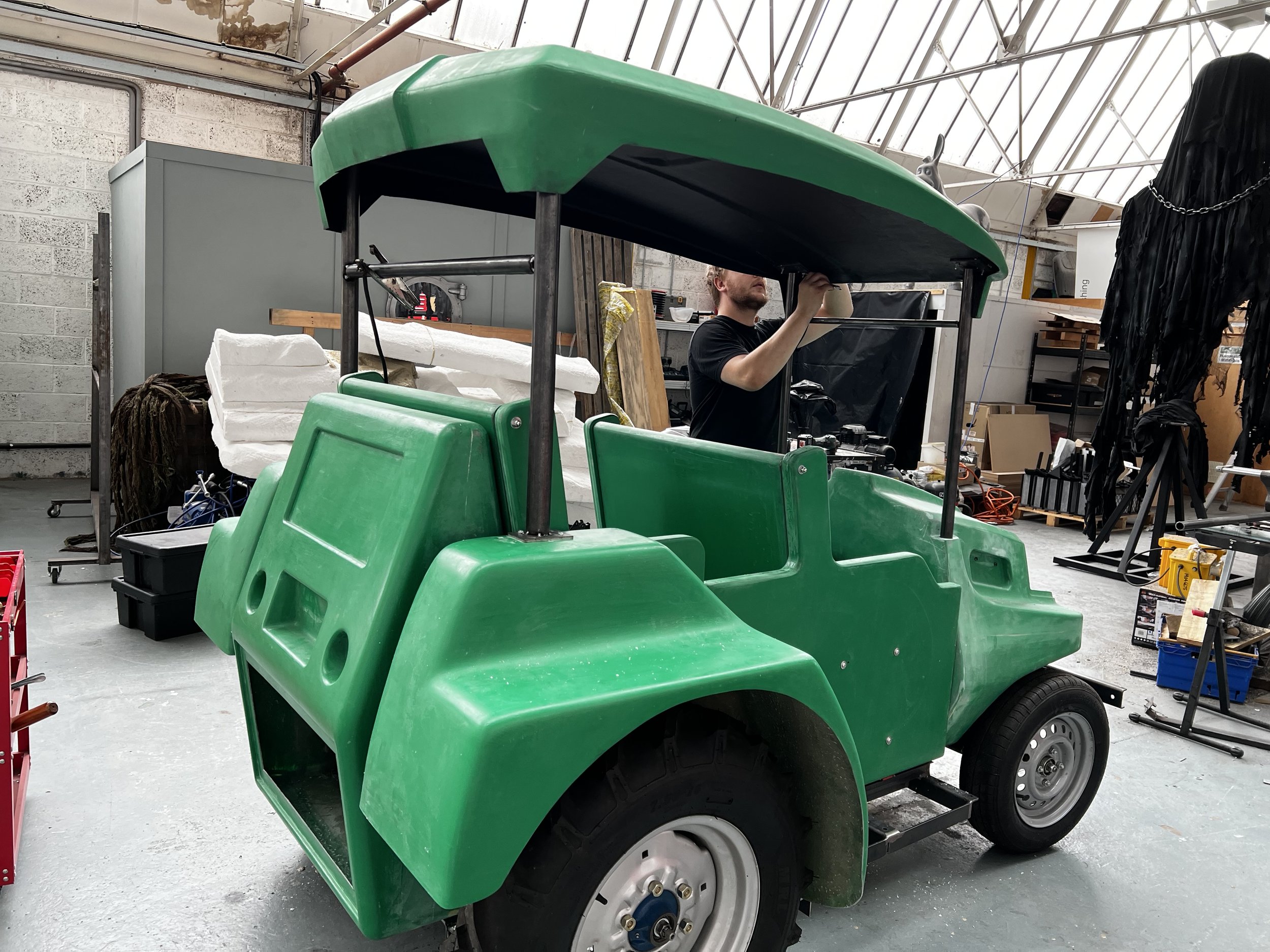 Person working on a green golf cart in a workshop