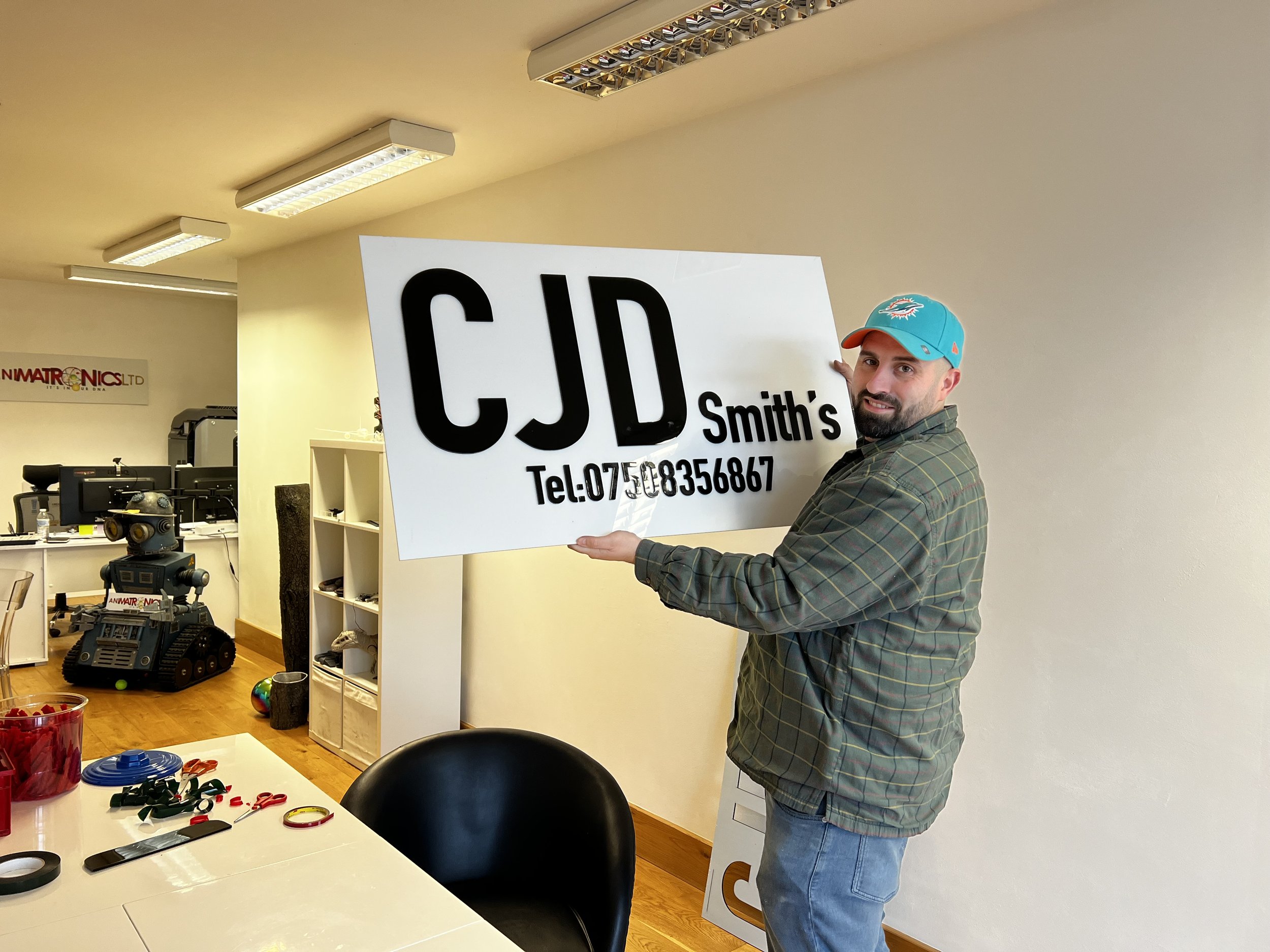 Man holding sign with text 'CJD Smith's' in an office setting.