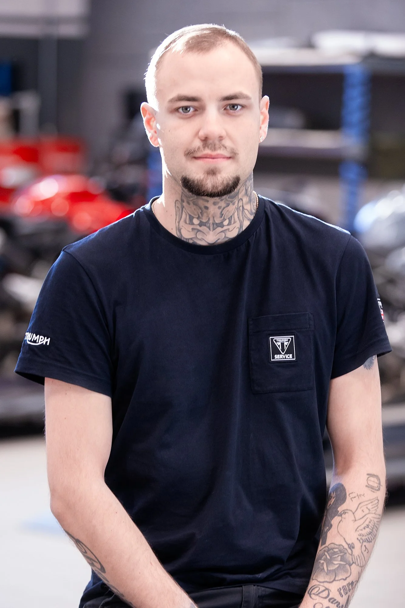 Person med tatueringar och svart Triumph-tröja i en verkstadsmiljö.