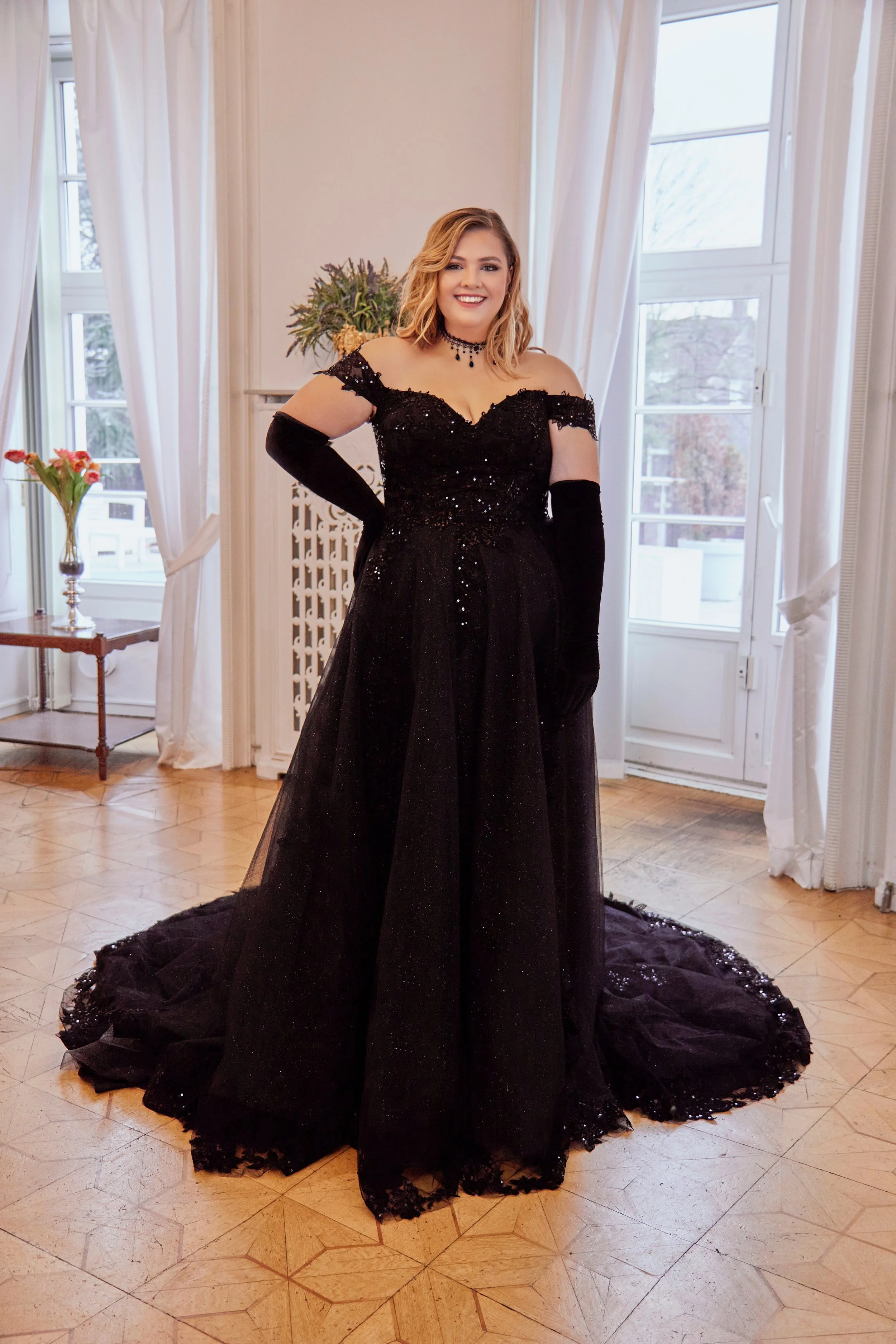 Full front view of Lia Bella Model Tiana, a black off-the-shoulder curvy wedding dress with a sparkling lace bodice and flowing A-line skirt.