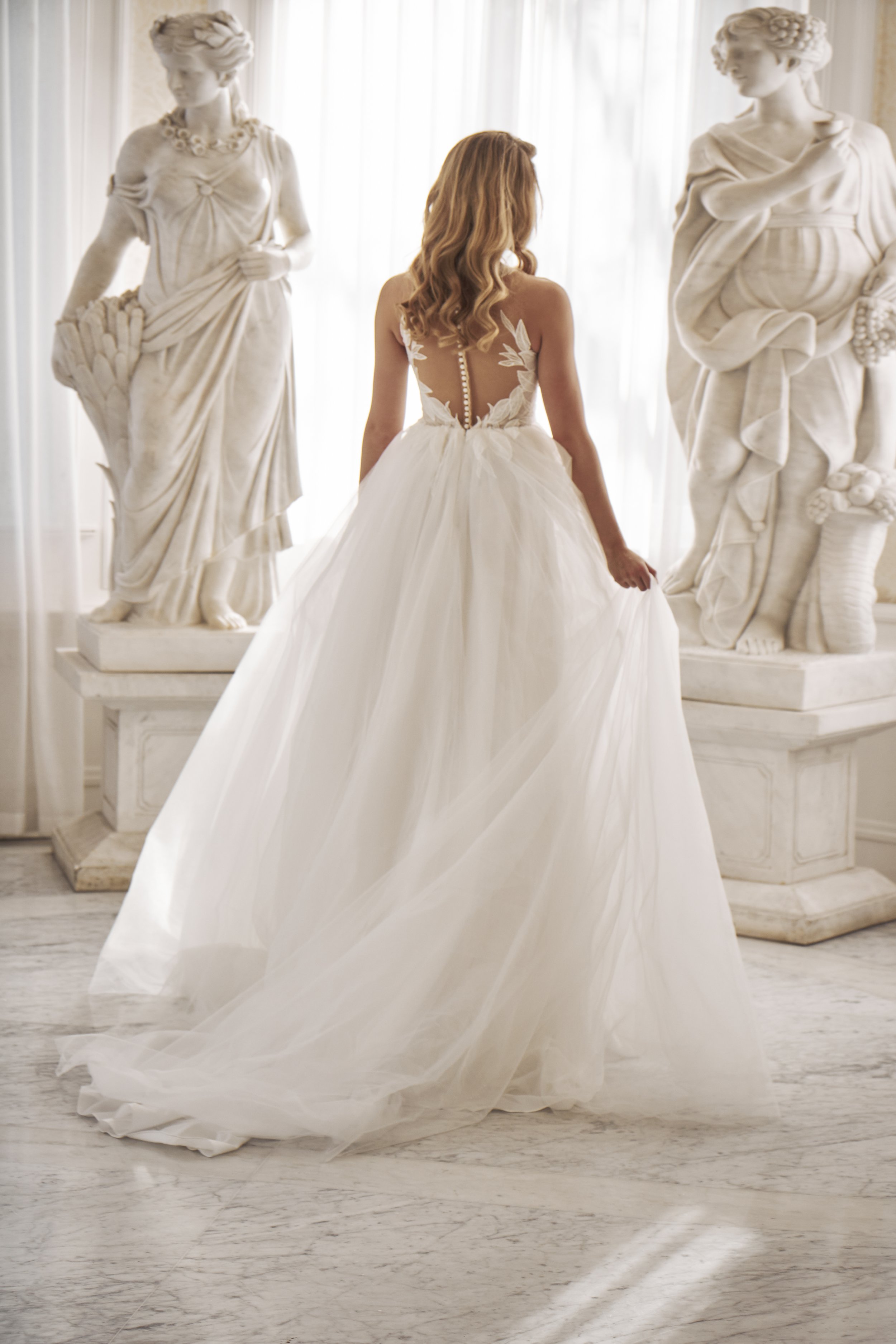 Back view of Lia Bella Model Tat showing the voluminous tulle skirt, illusion back and soft chapel train.