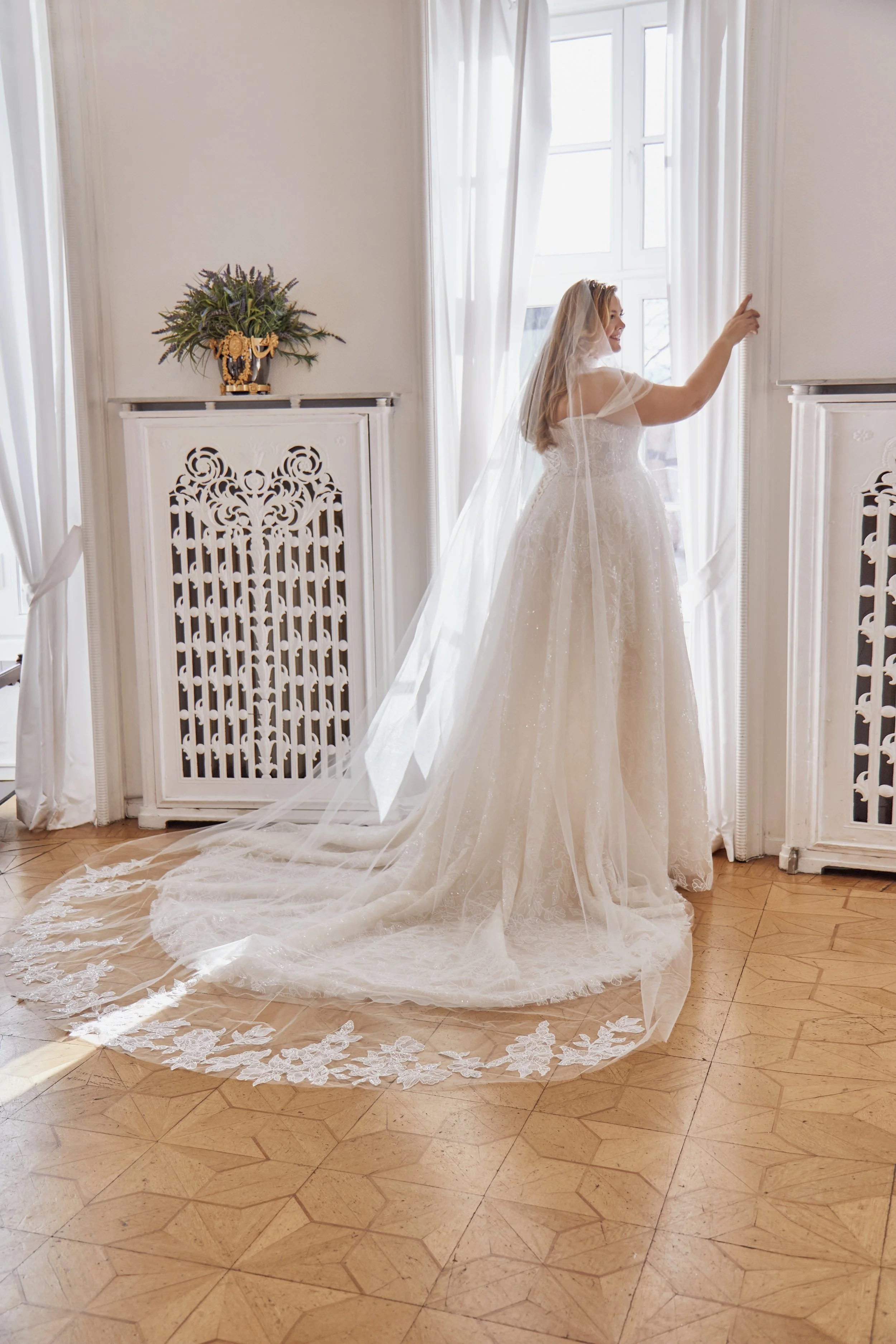 Three-quarter back view of Lia Bella Model Temea showing the embroidered lace skirt, structured back and soft sweep train.