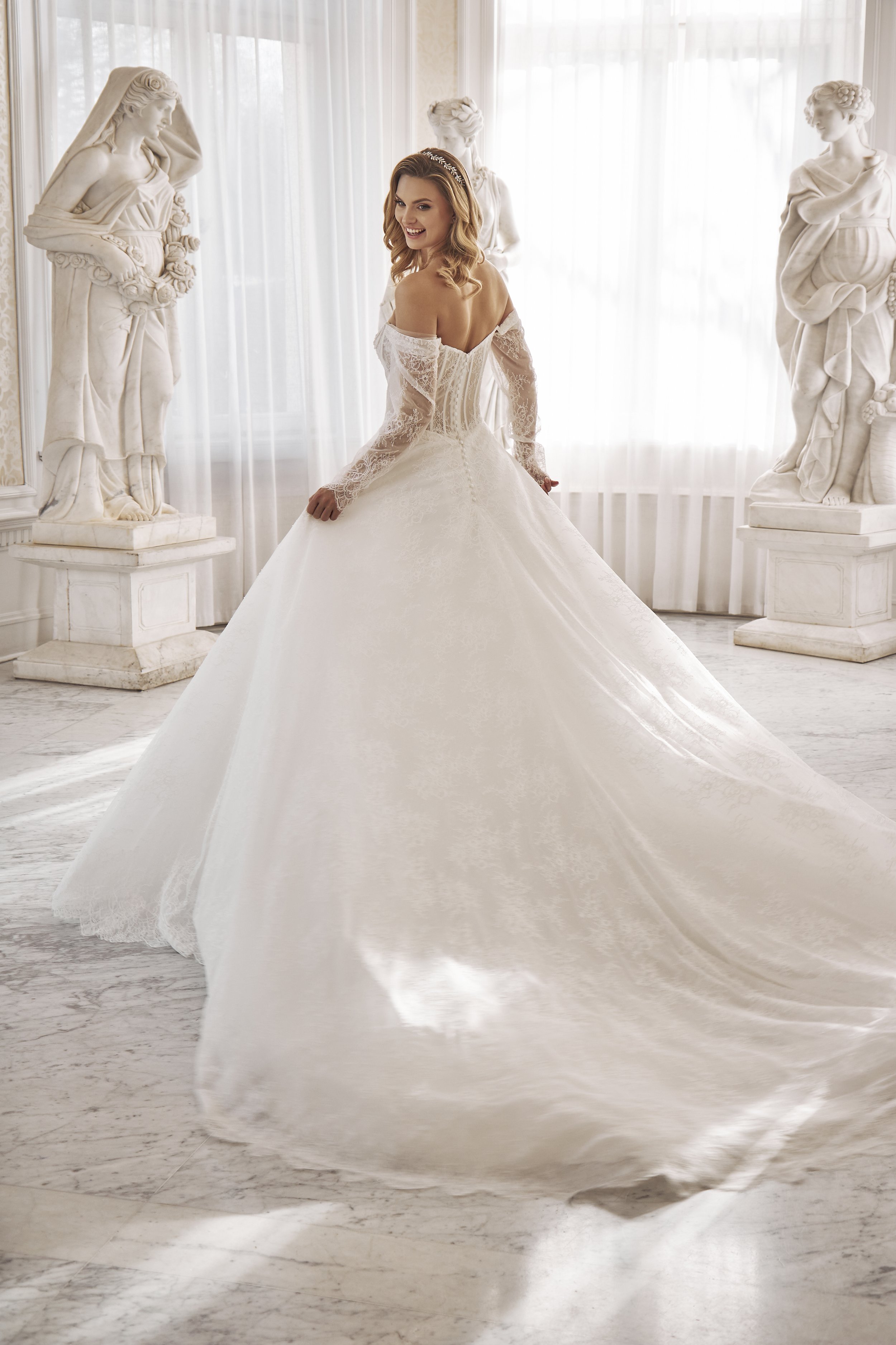 Bride in a romantic lace ball gown with off-the-shoulder sleeves among classical statues.