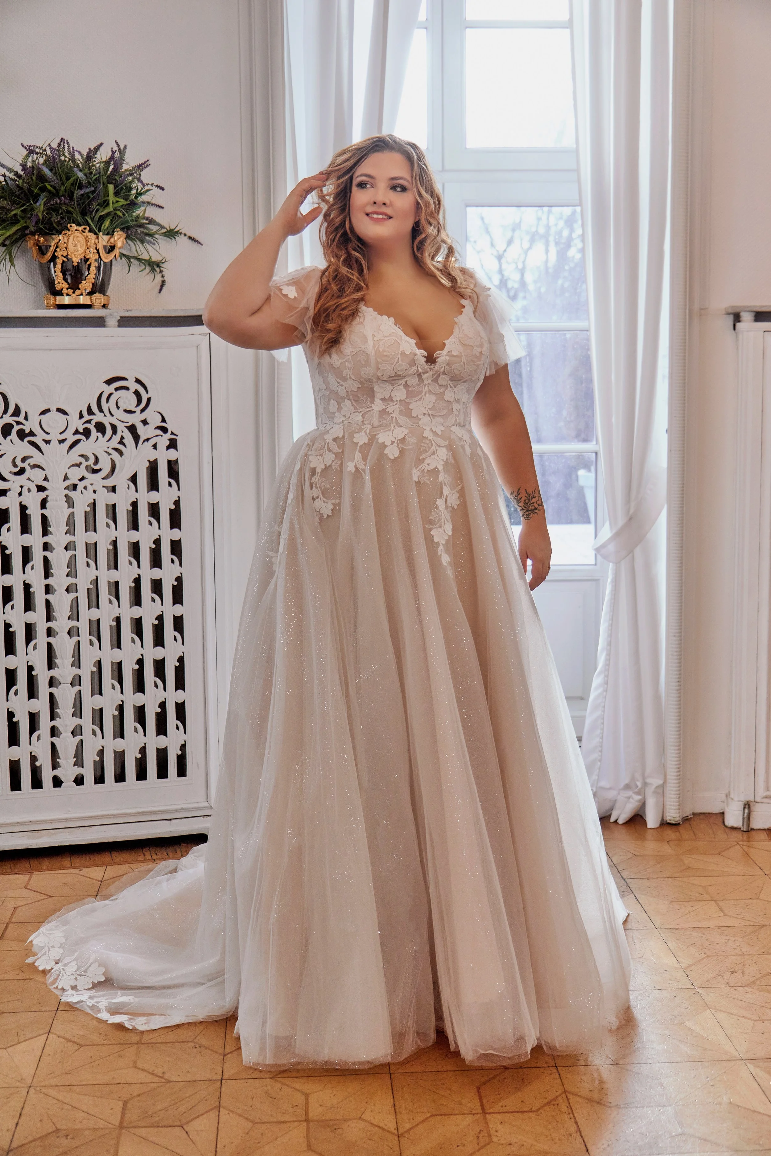 Lia Bella Model Tsuna, a curvy A-line wedding dress with a floral lace bodice, flutter sleeves and a glitter tulle skirt, shown from the front.
