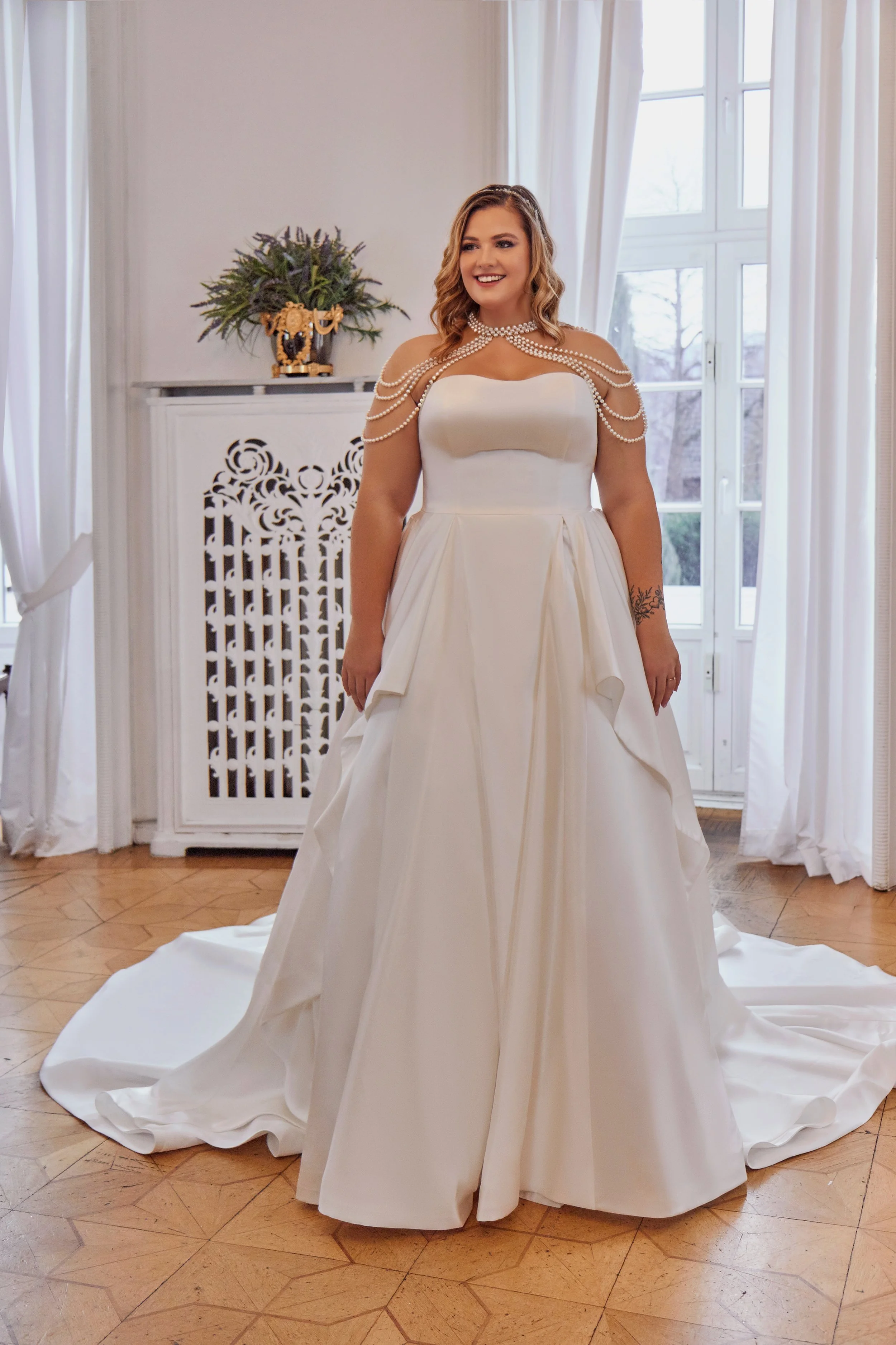 Full front view of Lia Bella Model Taty, a strapless curvy A-line wedding dress in structured satin with draped overskirt panels.