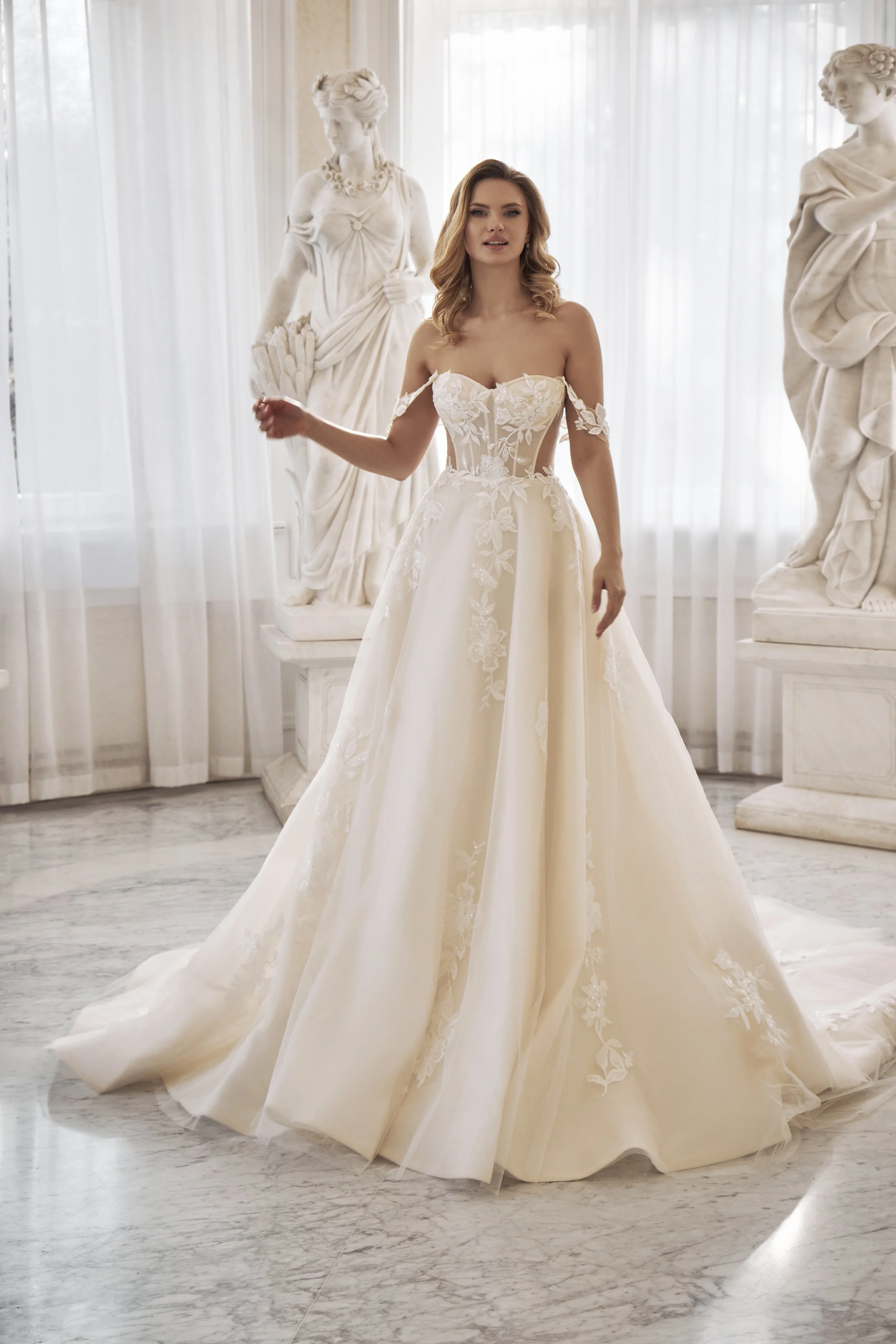 Full front view of Lia Bella Model Tamse, an off-the-shoulder ball gown wedding dress with a sheer corset bodice and floral lace.