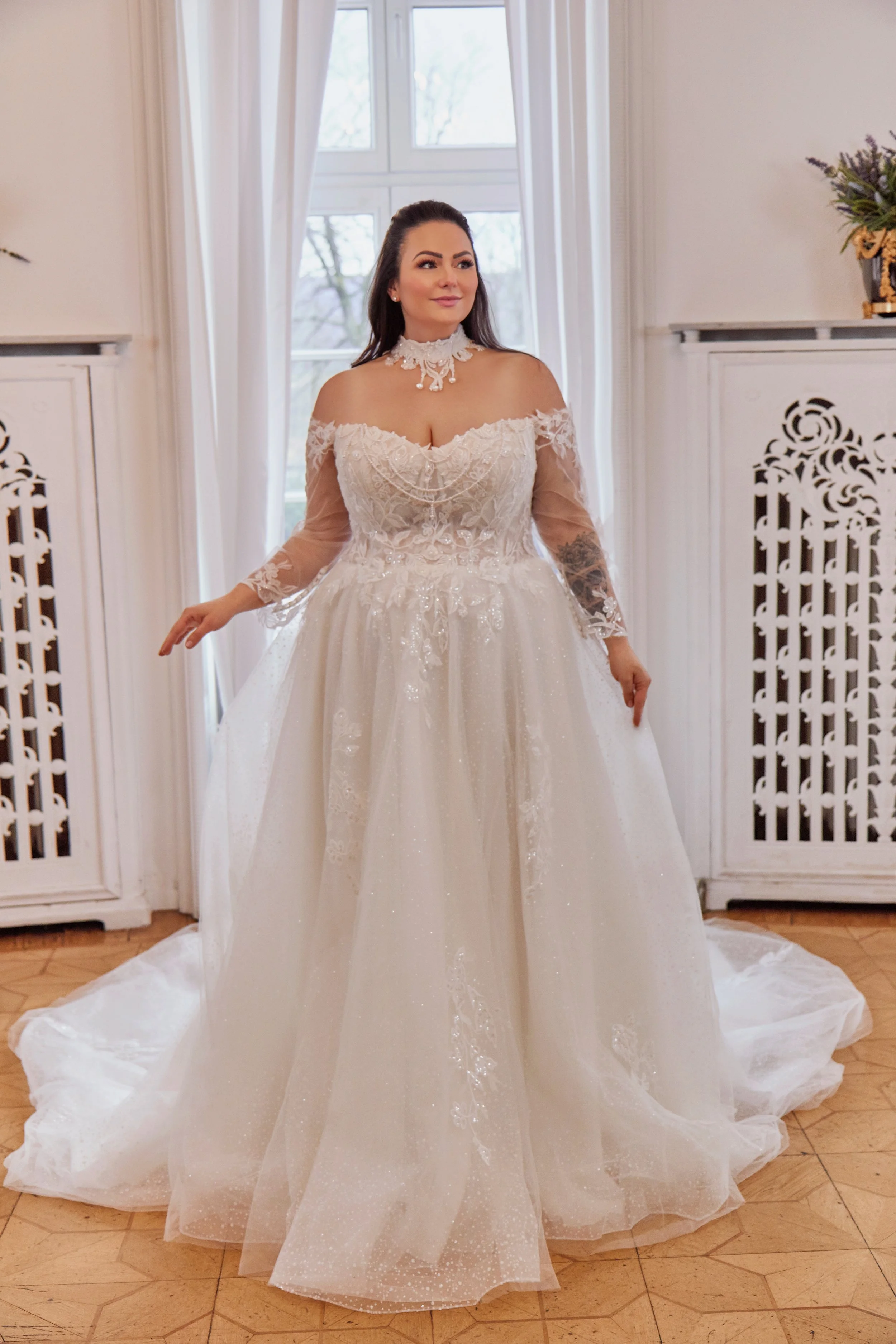 Full front view of Lia Bella Model Tulla, an off-the-shoulder curvy ball gown with long illusion sleeves, an ornate lace bodice and glitter-tulle skirt.