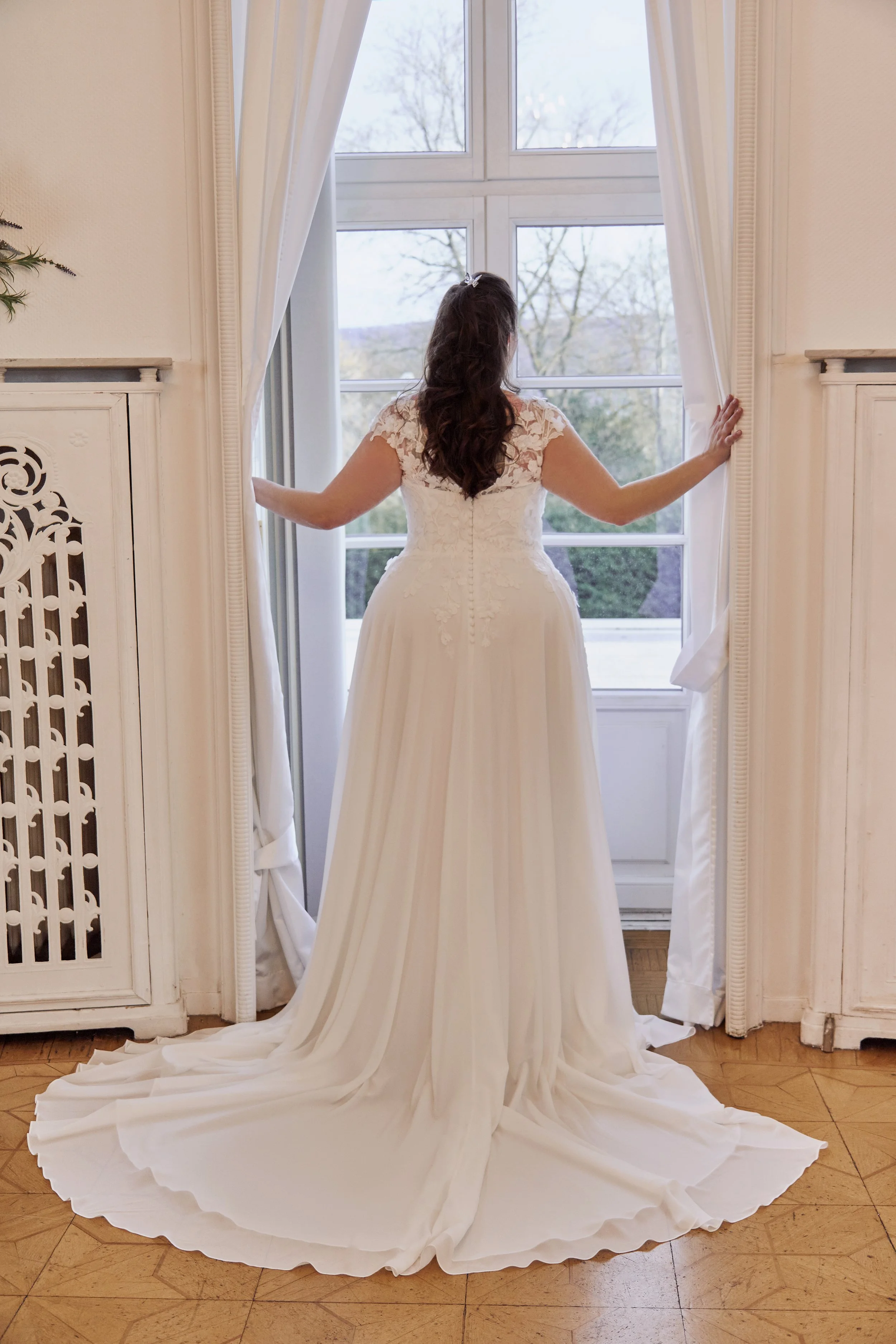 Back view of Lia Bella Model Toya showing the illusion lace back, covered buttons and flowing chiffon chapel train.