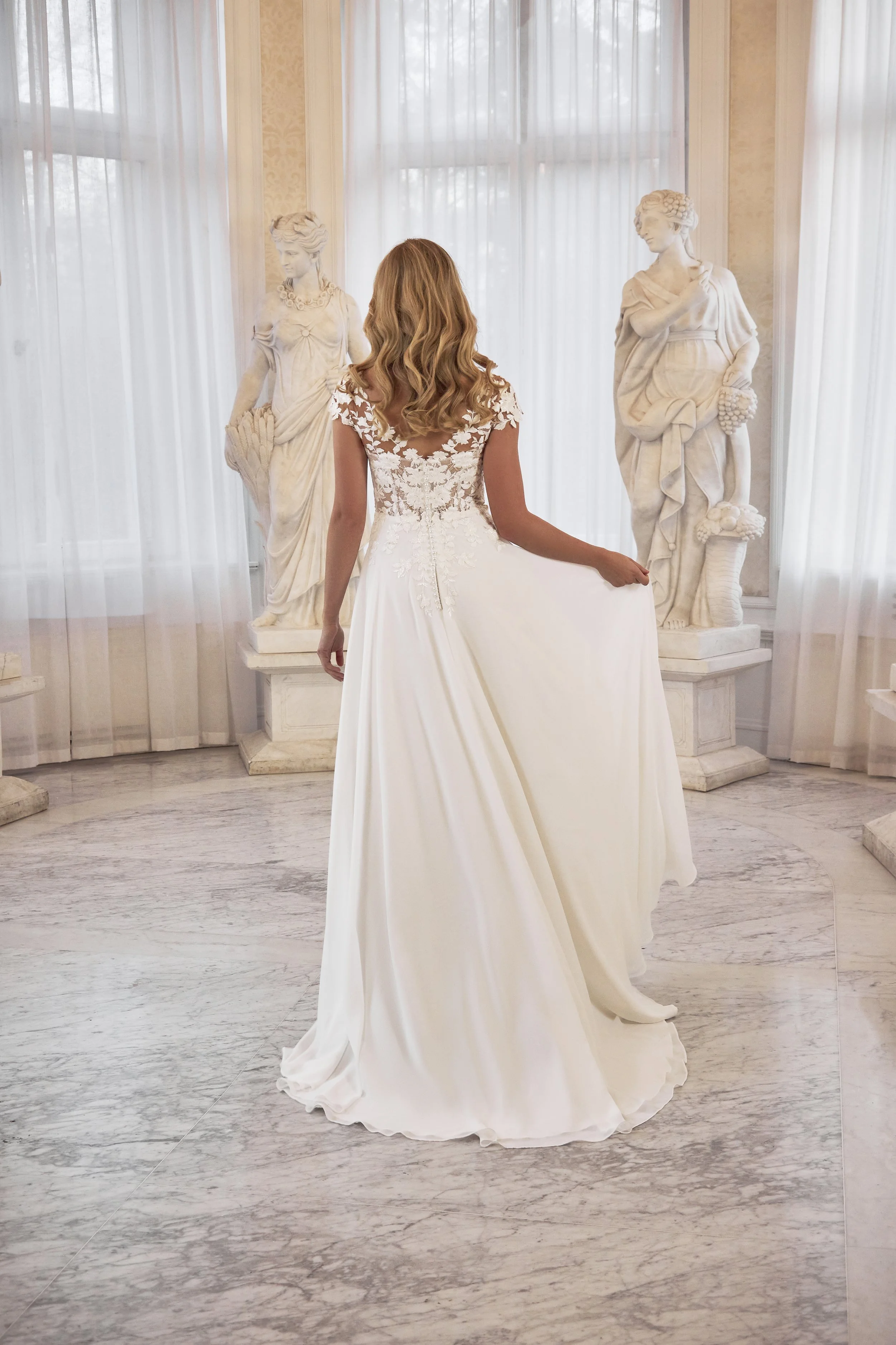 Full back view of Lia Bella Model Terra showing the illusion lace back, covered buttons and flowing chiffon skirt.
