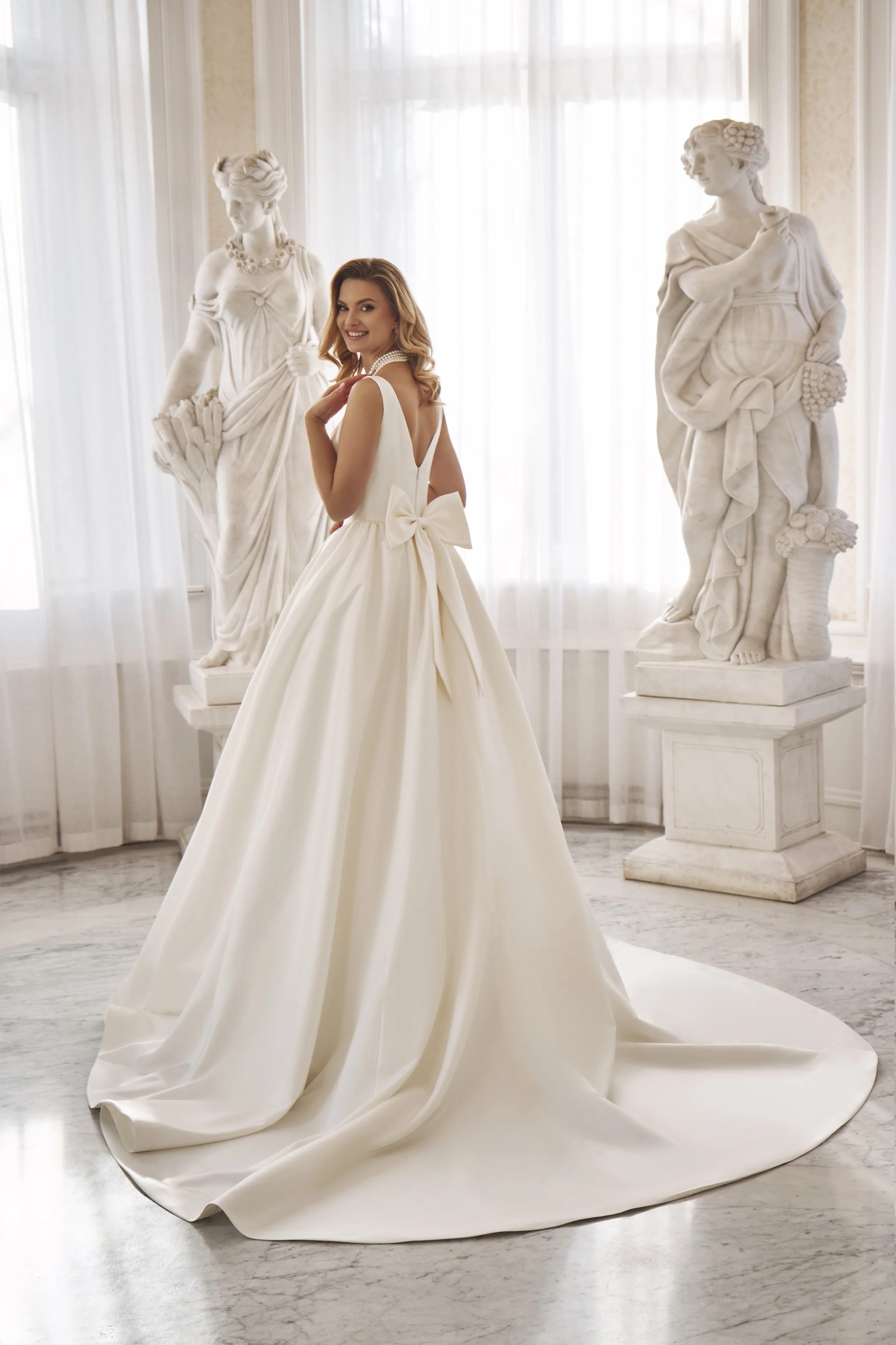 Full back view of Lia Bella Model Toshi showing the low V-back, oversized satin bow and sweeping chapel train.