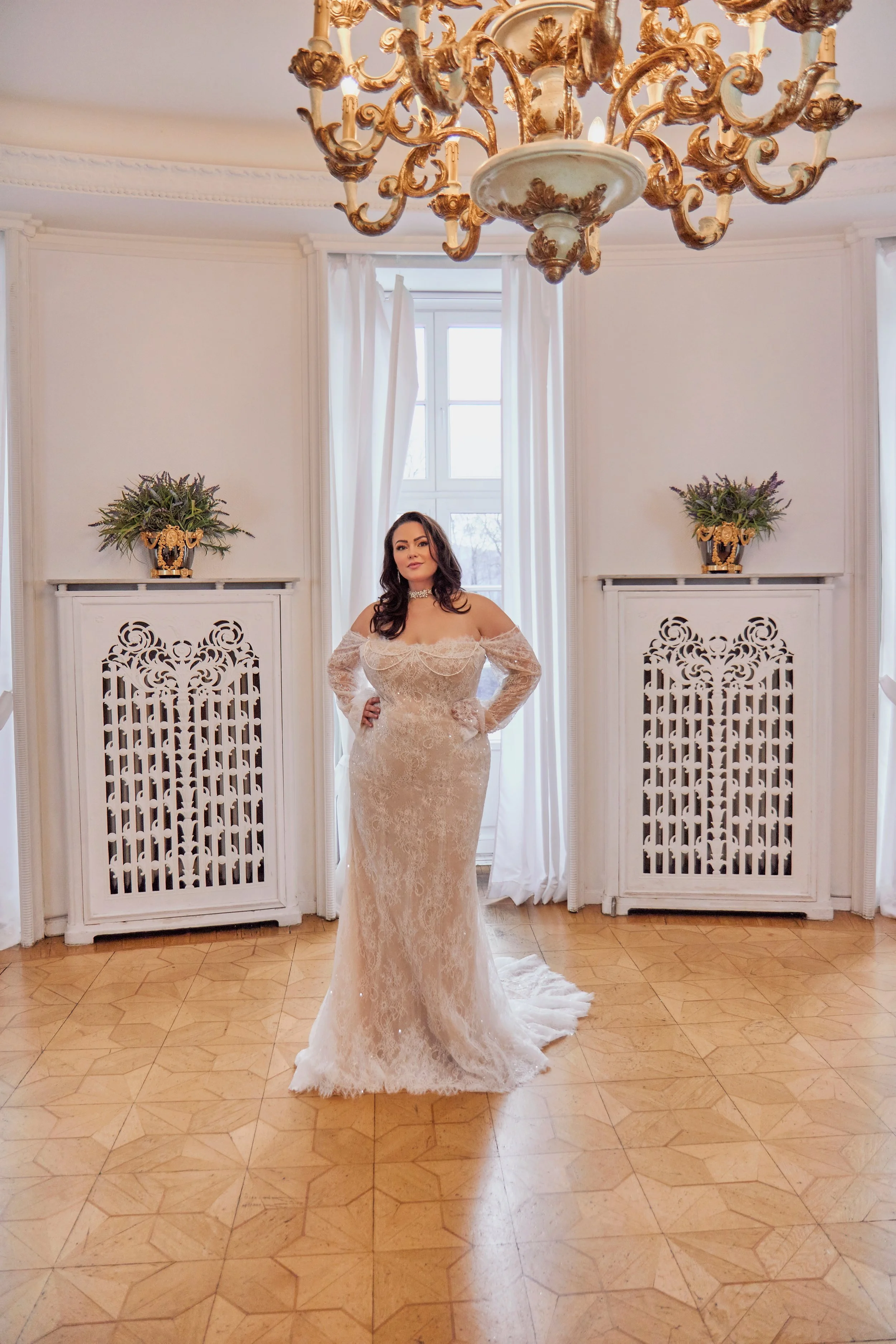 Full front view of Lia Bella Model Tiffania, a curvy lace fit-and-flare wedding dress with an off-the-shoulder neckline and long sleeves.
