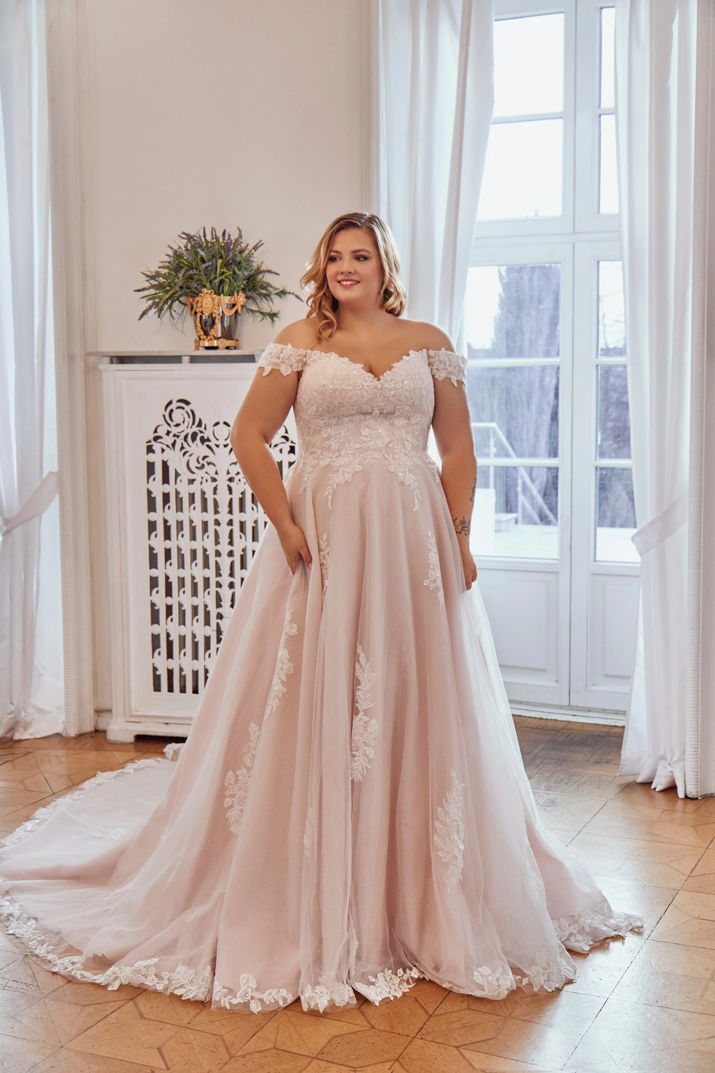 Full front view of Lia Bella Model Tasmine, an off-the-shoulder curvy A-line wedding dress with floral lace and a flowing tulle skirt.