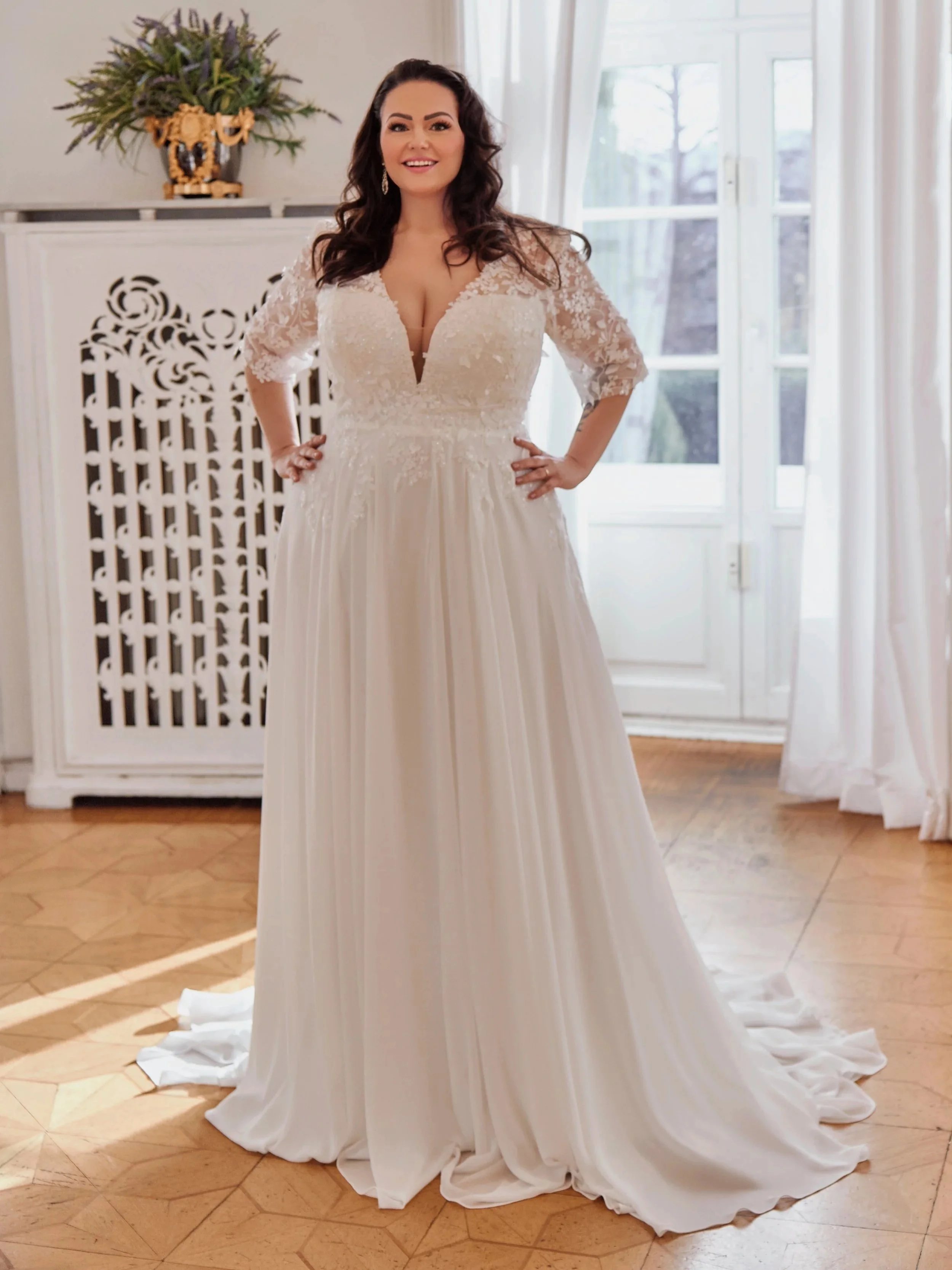 Full front view of Lia Bella Model Trinity, a curvy A-line wedding dress with a deep V-neckline, floral lace bodice and three-quarter illusion sleeves.