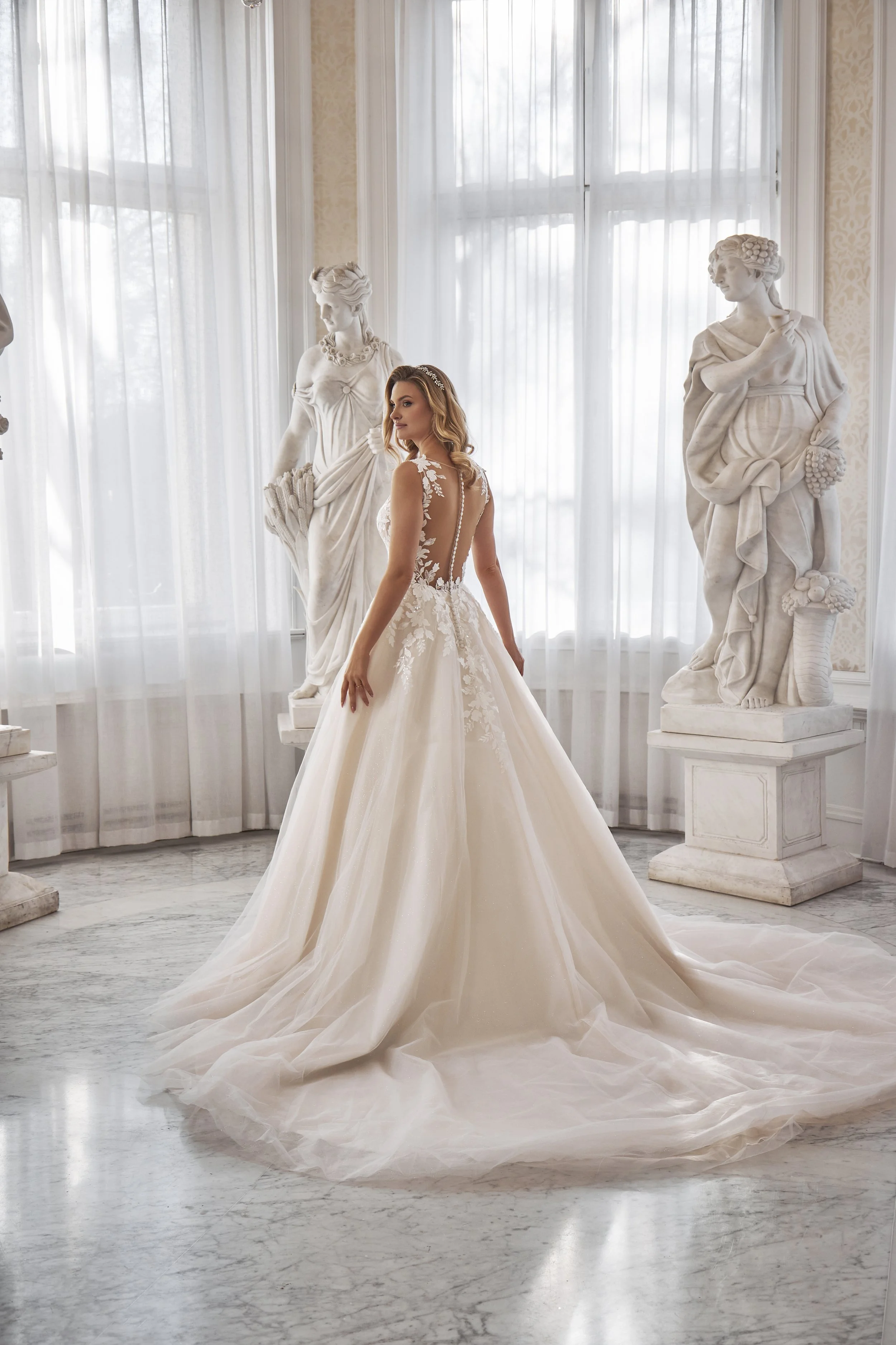 Back view of Lia Bella Model Tarja showing the buttoned illusion back, layered tulle skirt and flowing train.