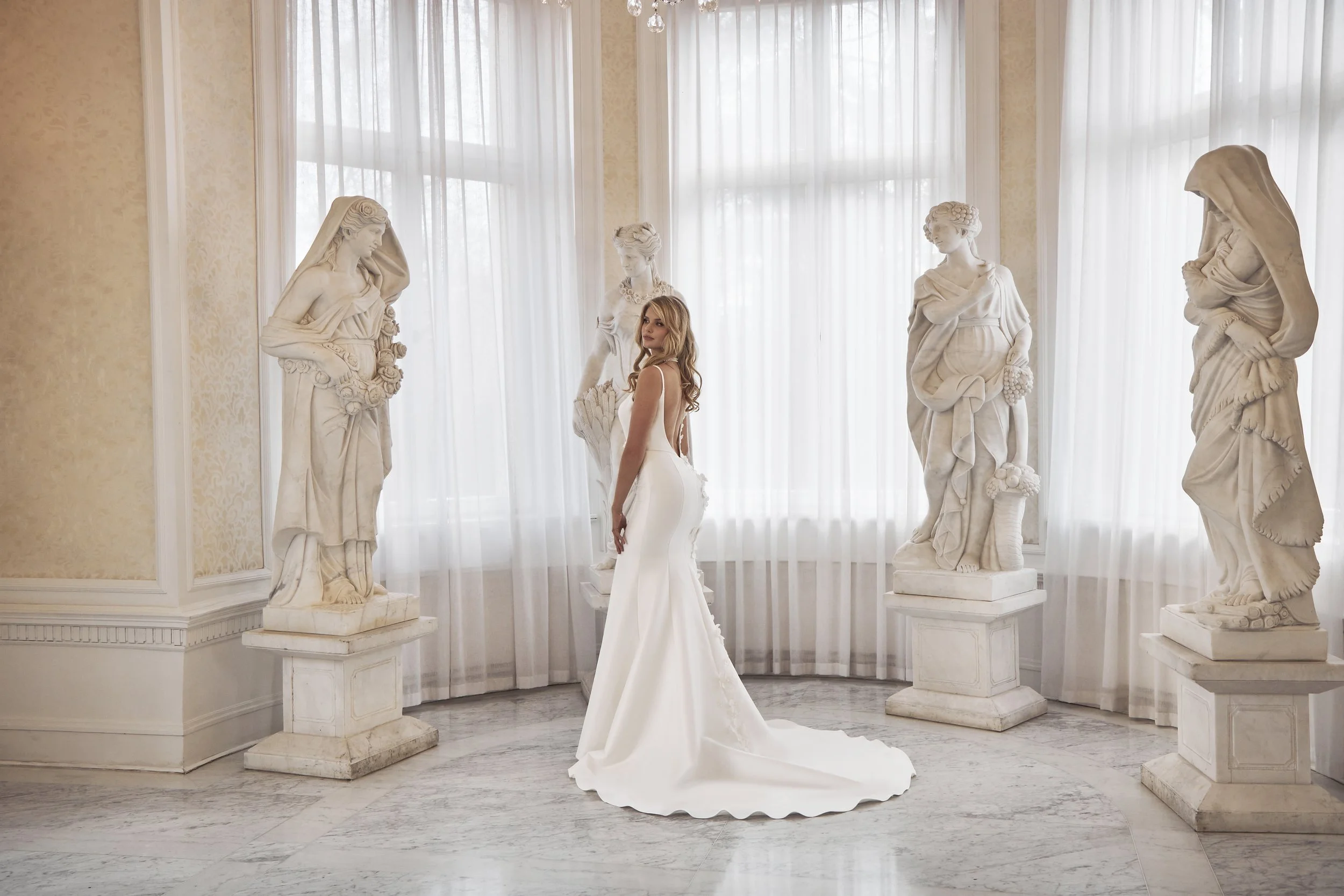 Bride in a modern fitted Lia Bella wedding dress surrounded by classical statues.