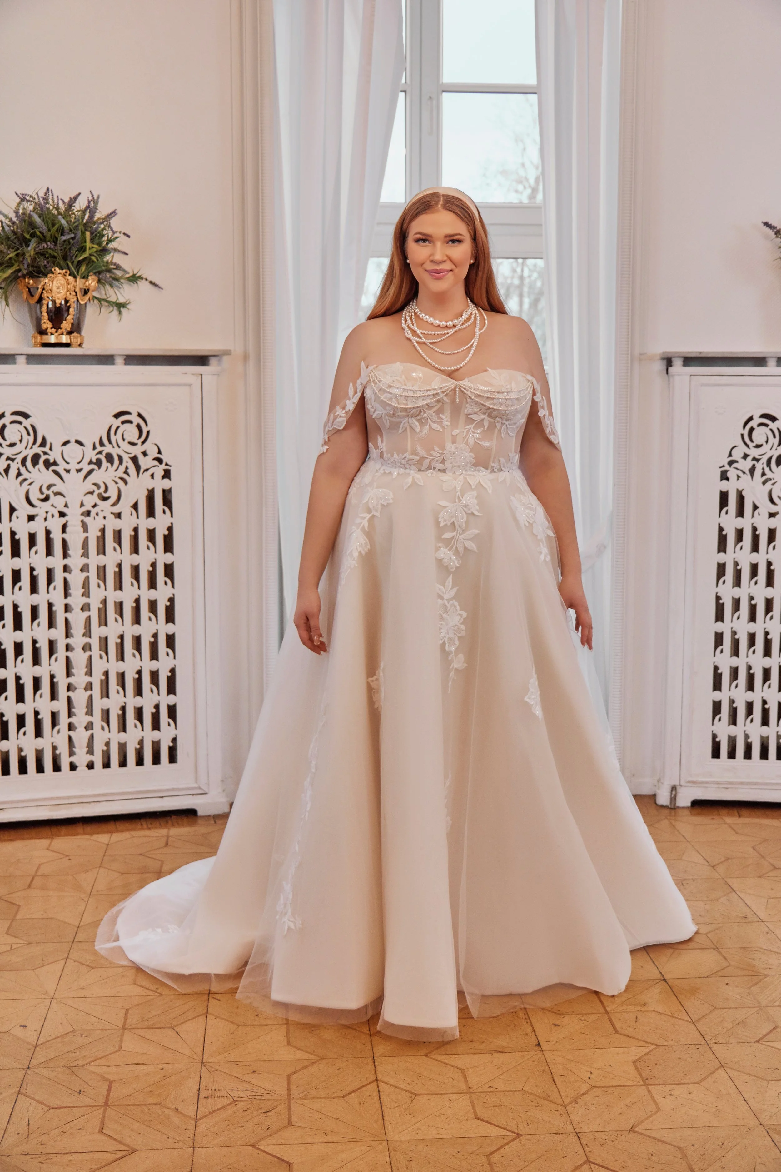 Full front view of Lia Bella Model Tazia, a curvy A-line wedding dress with an illusion lace corset, off-the-shoulder straps and pearl detailing.