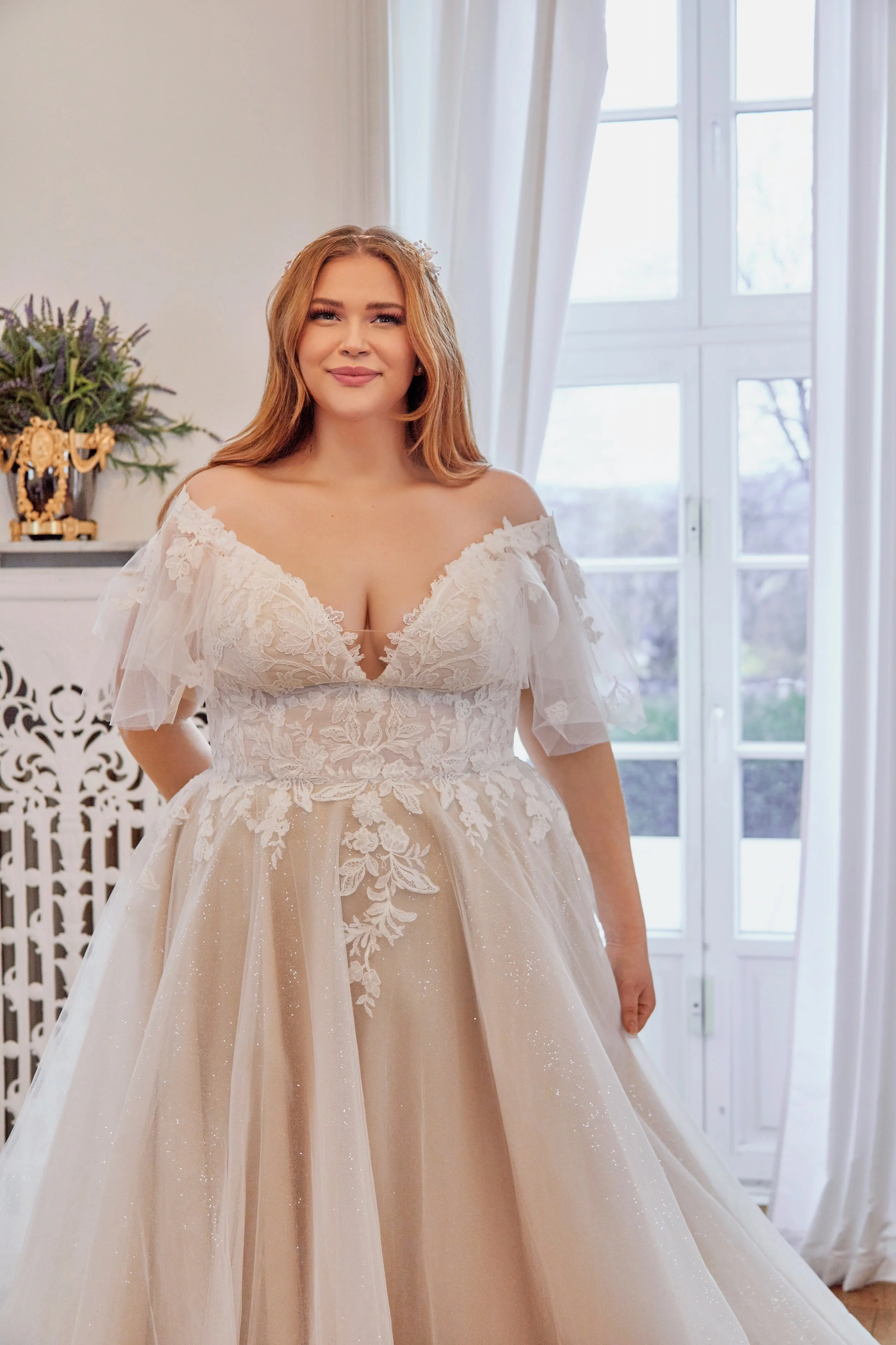 Close-up of Lia Bella Model Tewa highlighting the plunging V-neckline, floral lace bodice and off-the-shoulder tulle sleeves.