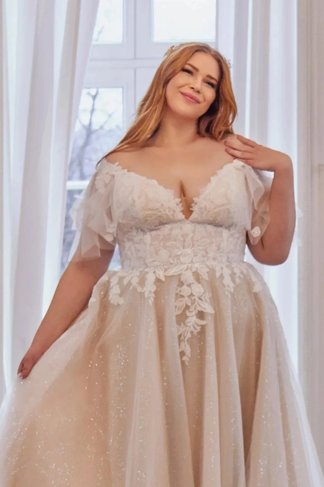 Full front view of Lia Bella Model Tewa, a curvy A-line wedding dress with a floral lace bodice, flutter sleeves and shimmering tulle skirt.