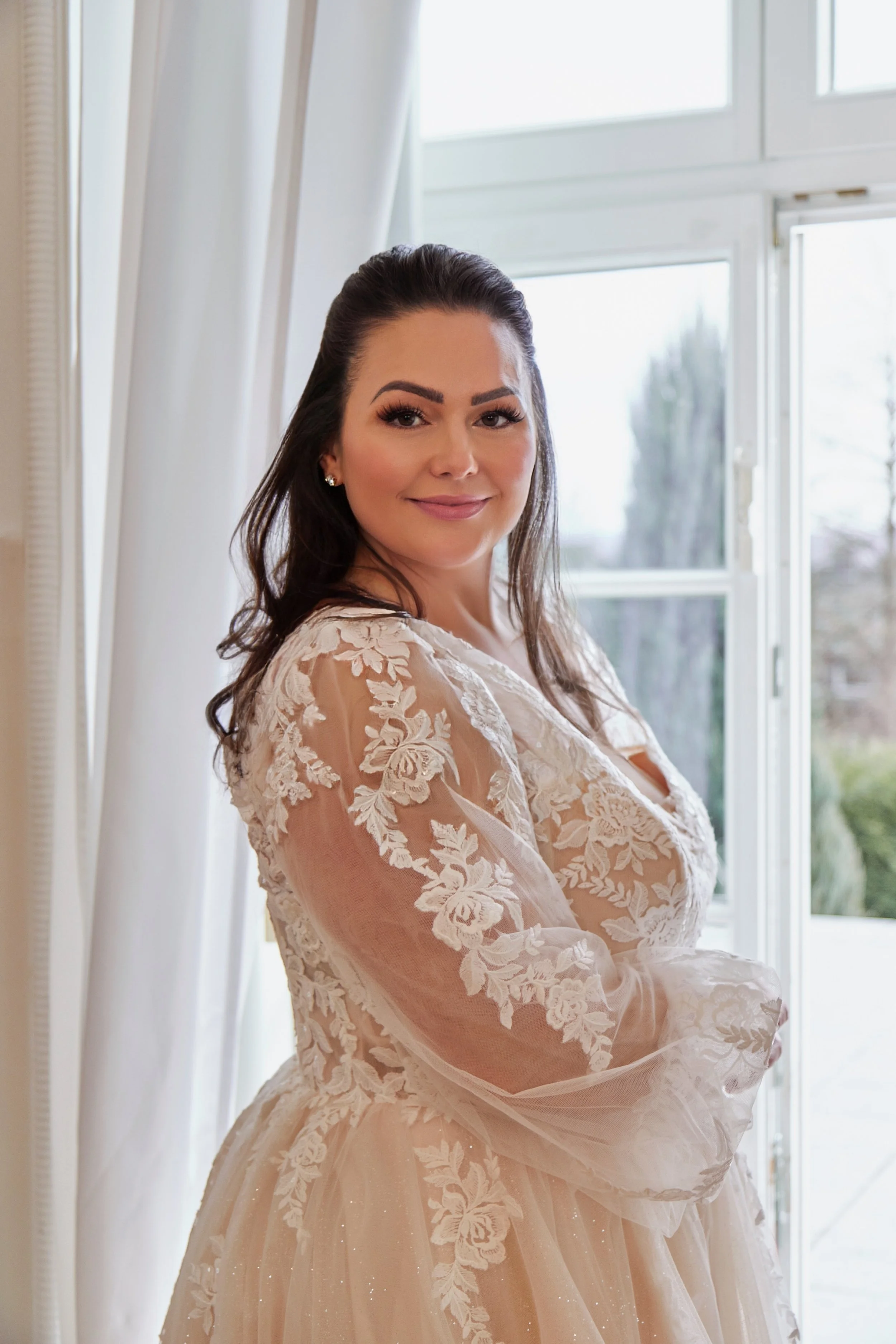 Side detail of Lia Bella Model Tiede featuring a transparent long sleeve with floral lace appliqués and a softly flared cuff.