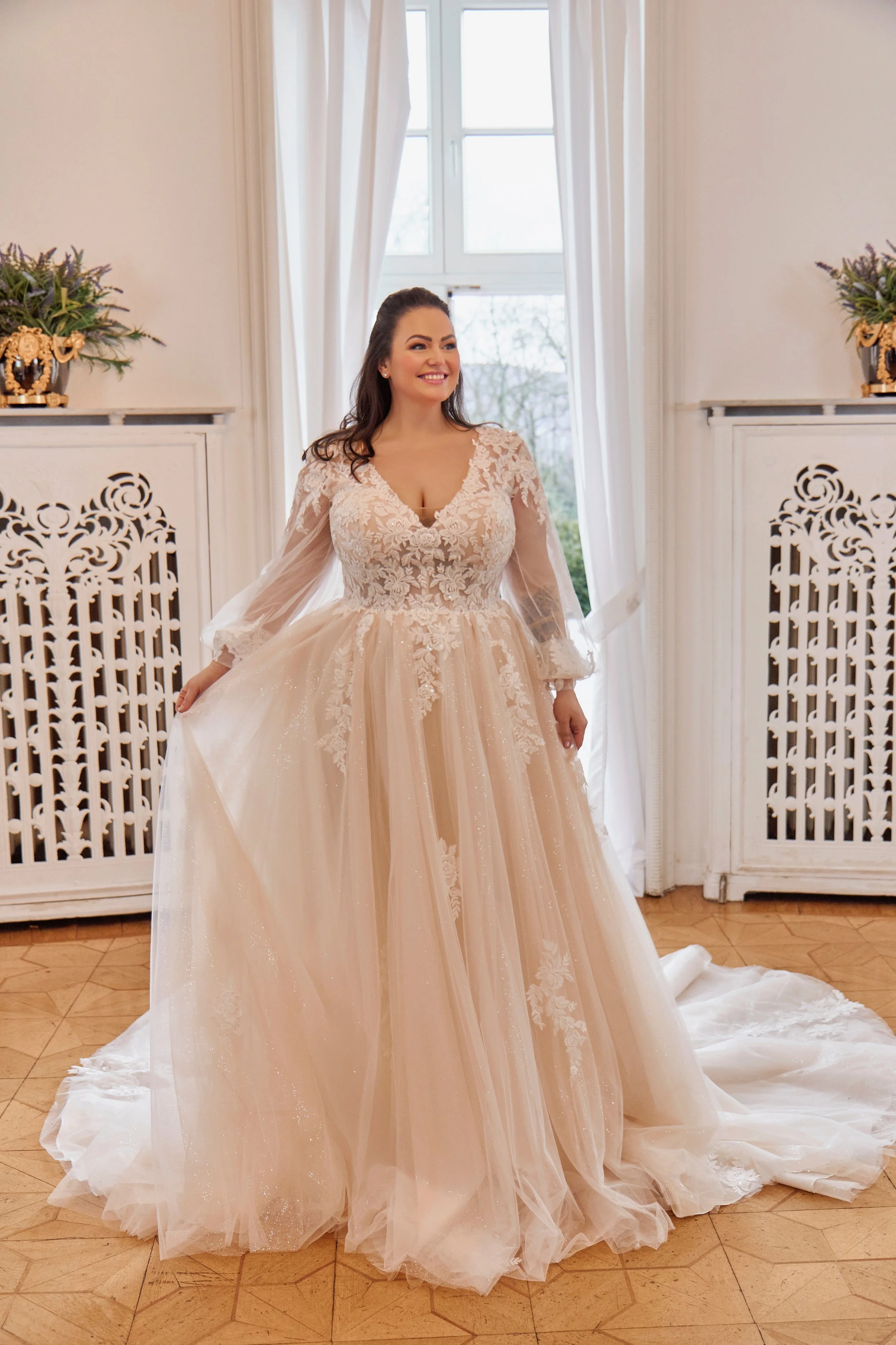 Full front view of Lia Bella Model Tiede, a long-sleeve curvy A-line wedding dress with floral lace and a glitter-tulle skirt.
