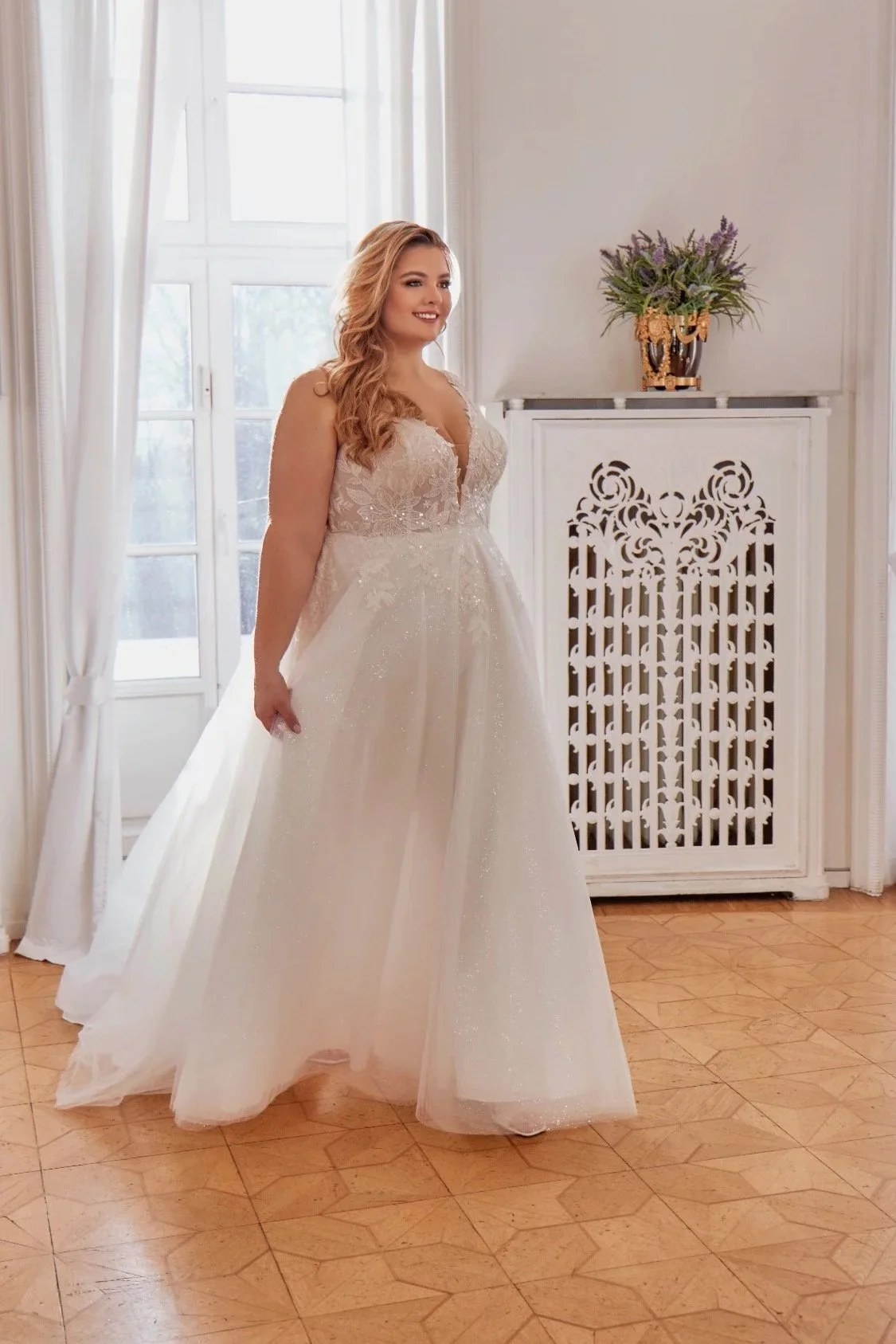 Full front view of Lia Bella Model Trudy, a glitter-tulle curvy A-line wedding dress with a deep V-neckline and floral lace bodice.
