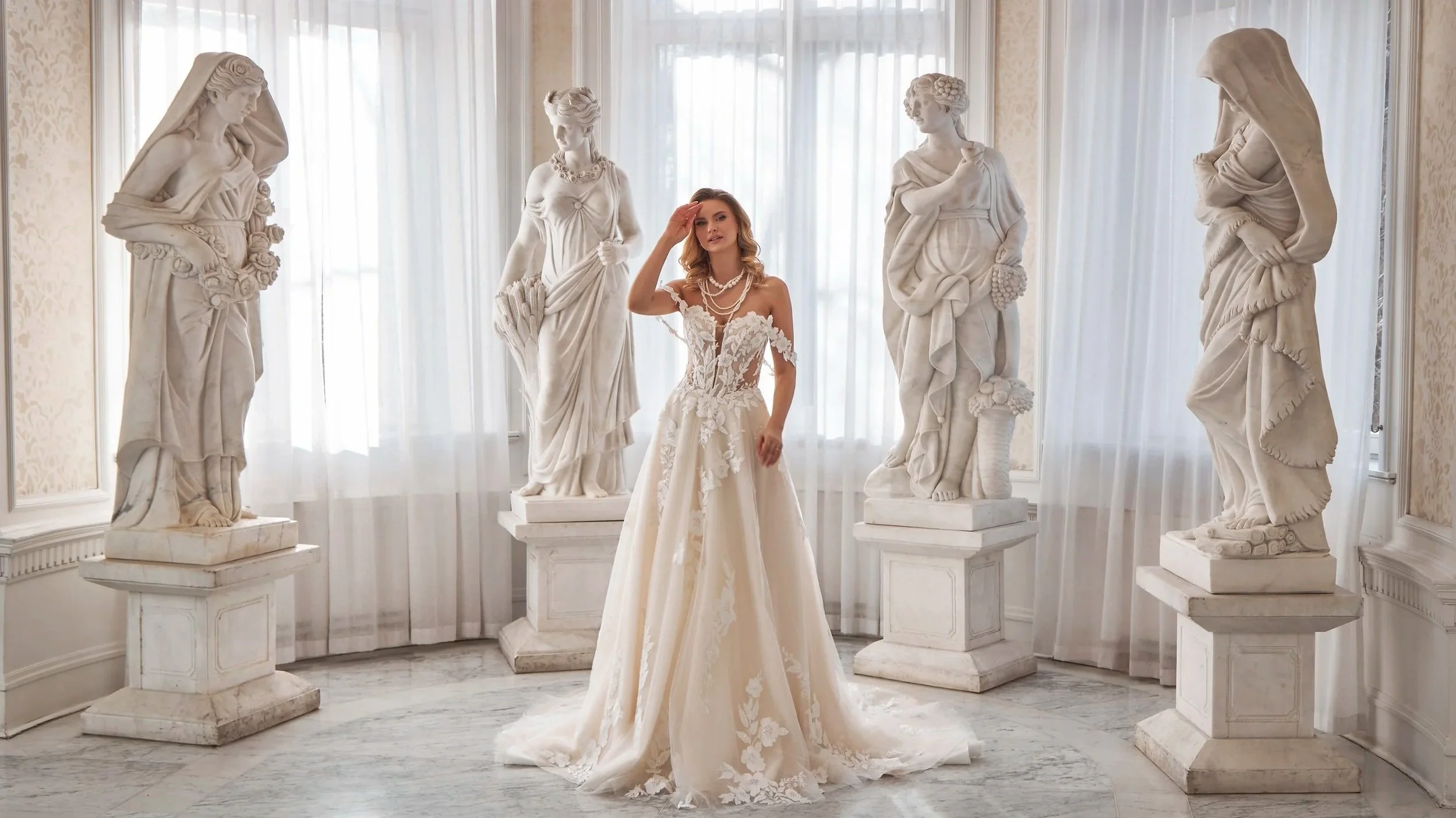 Bride in an ivory lace wedding dress standing among classical statues