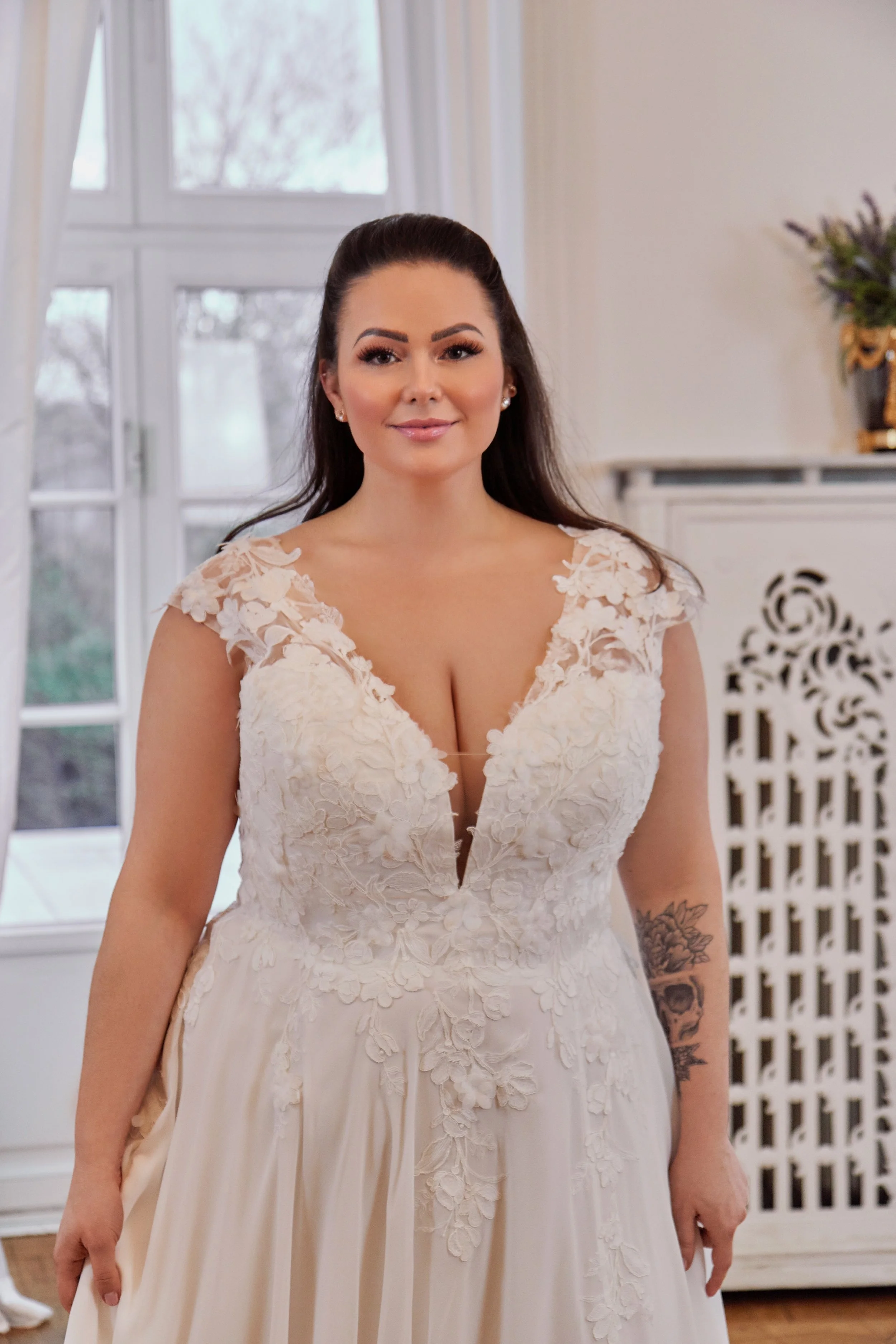 Close-up of Lia Bella Model Toya highlighting the deep V-neckline, illusion inset and floral lace cap sleeves.